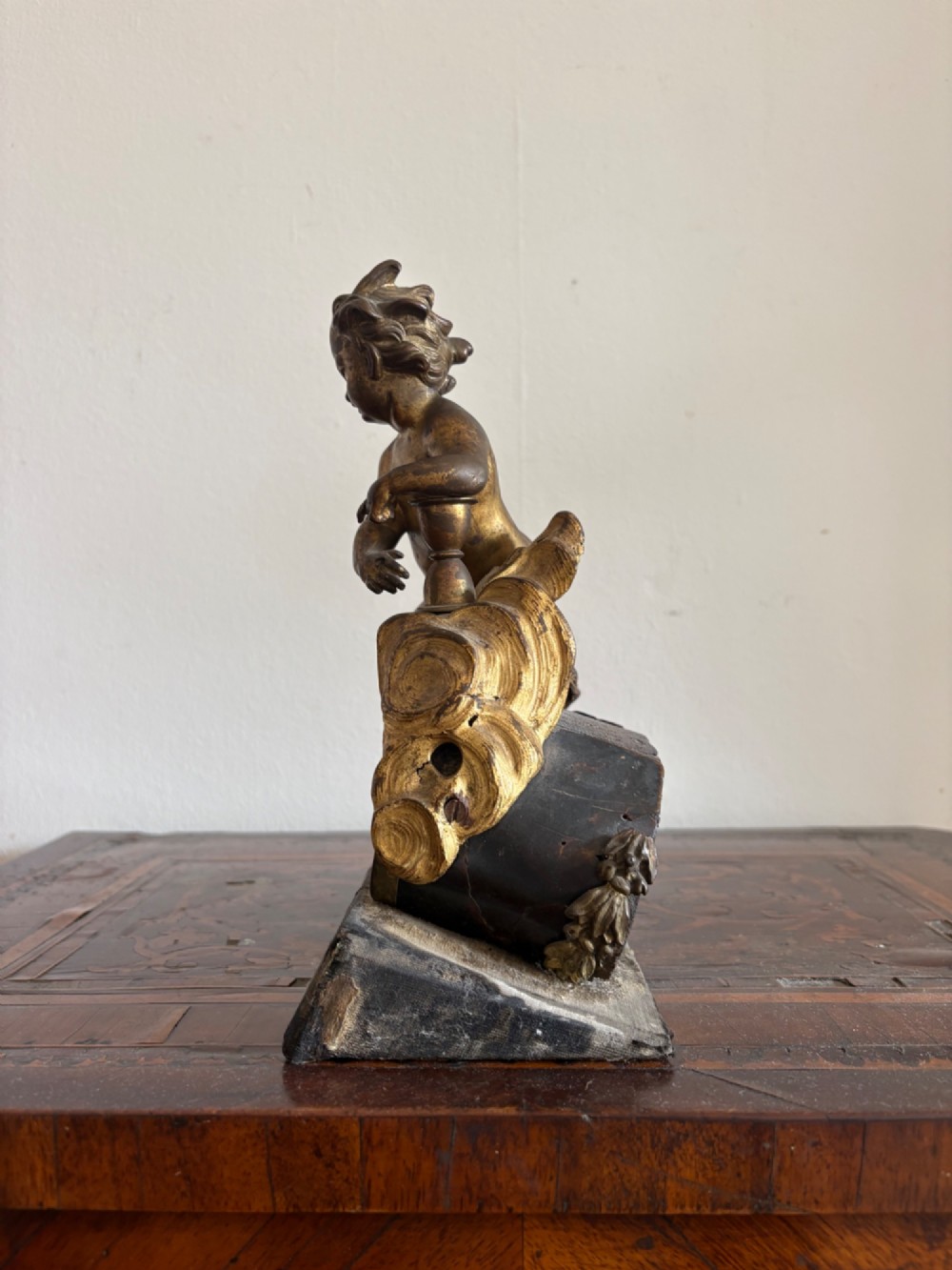 A late eighteenth or nineteenth-century French gilt bronze ormolu sculpture featuring a reclining putto holding a small vessel above a scrolled arch base. View V