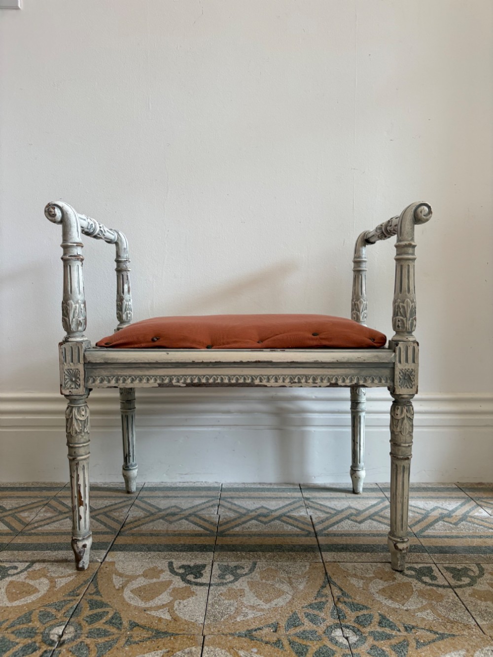 A white painted Gustavian style stool featuring raised side handles, fluted legs, and a terracotta silk upholstered seat. View II
