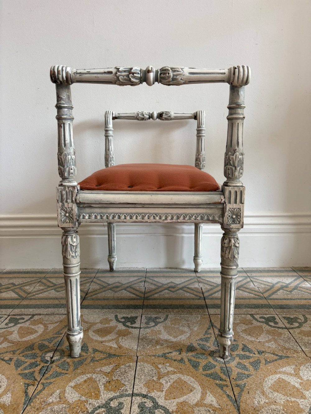 A white painted Gustavian style stool featuring raised side handles, fluted legs, and a terracotta silk upholstered seat. View X