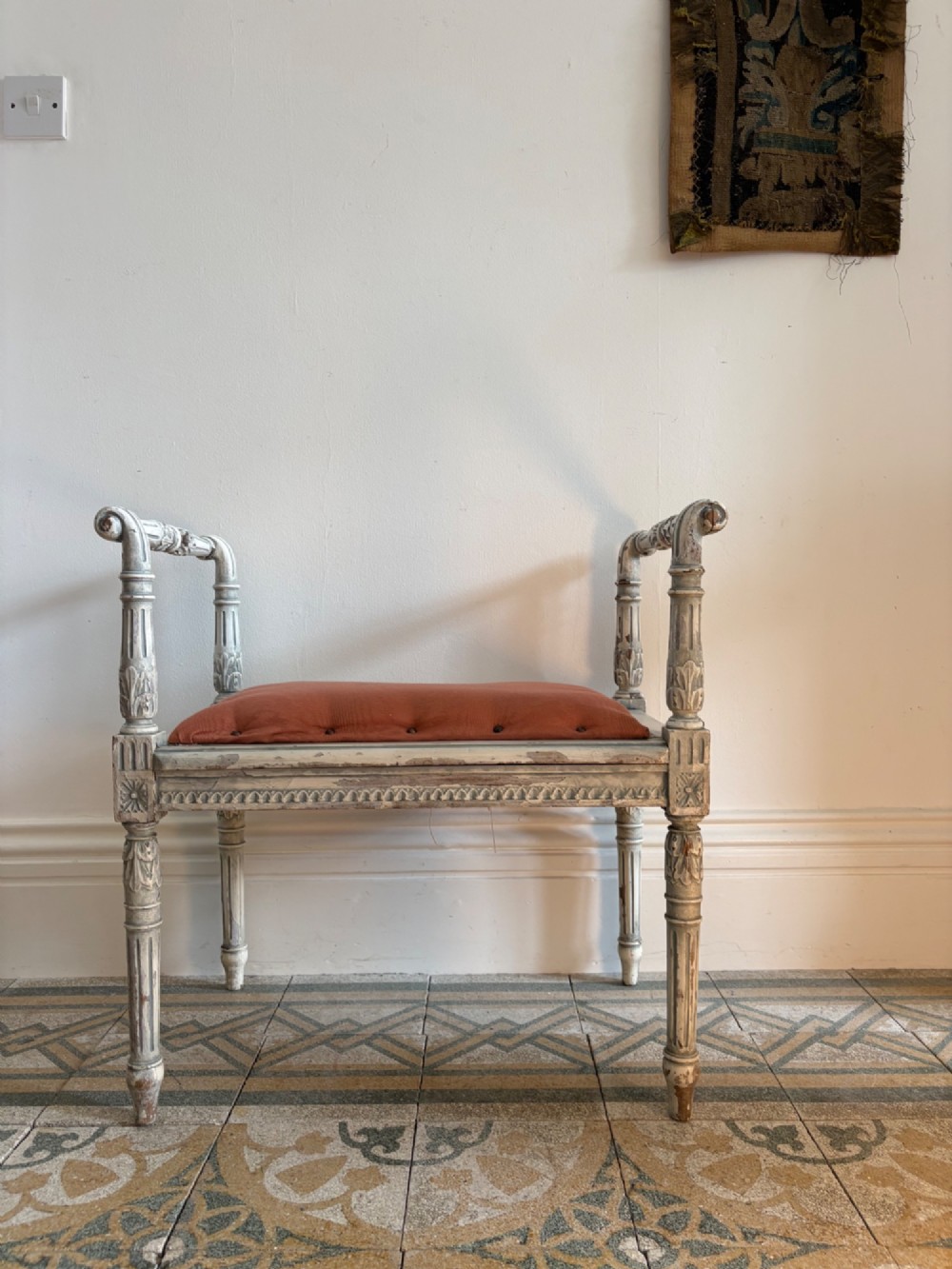 A white painted Gustavian style stool featuring raised side handles, fluted legs, and a terracotta silk upholstered seat.