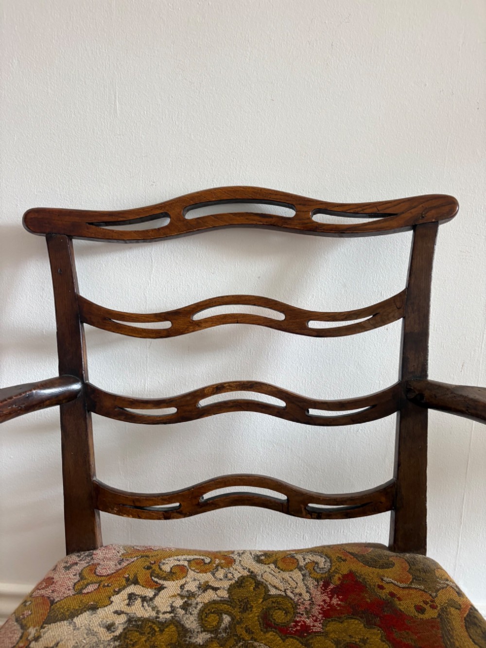 A George III elm ladderback open armchair featuring scrolled armrests and a patterned upholstered seat with fringed trim. View II