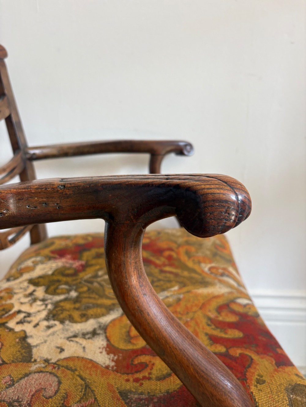 A George III elm ladderback open armchair featuring scrolled armrests and a patterned upholstered seat with fringed trim. View IV