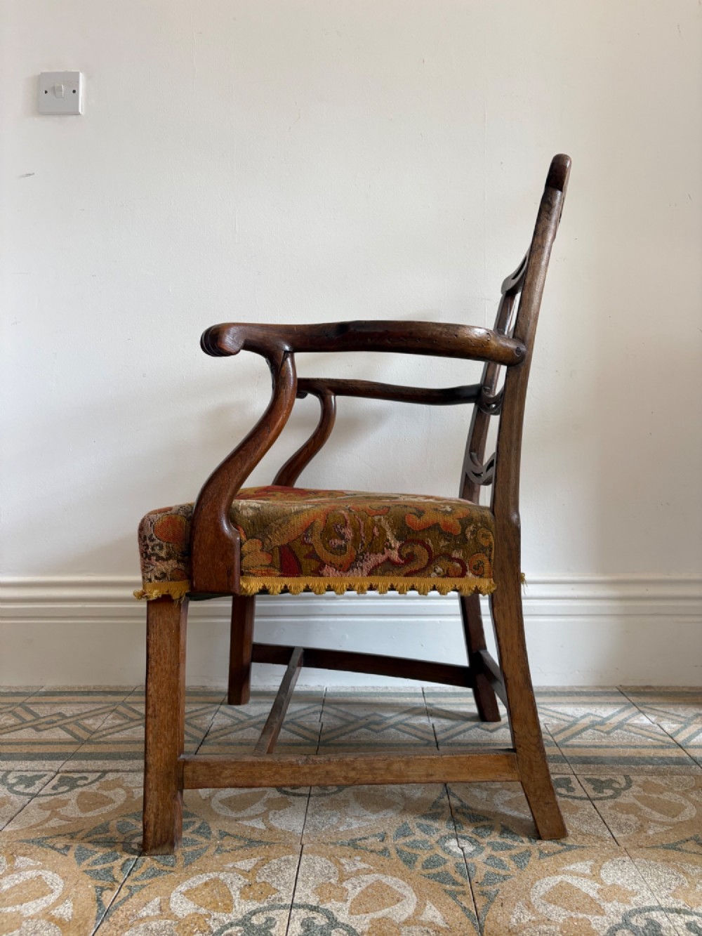 A George III elm ladderback open armchair featuring scrolled armrests and a patterned upholstered seat with fringed trim. View VI