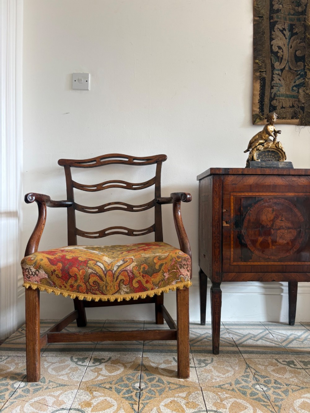 A George III elm ladderback open armchair featuring scrolled armrests and a patterned upholstered seat with fringed trim. View X