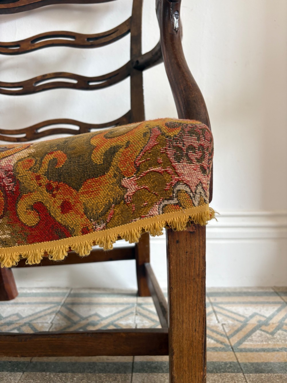 A George III elm ladderback open armchair featuring scrolled armrests and a patterned upholstered seat with fringed trim. View XIII