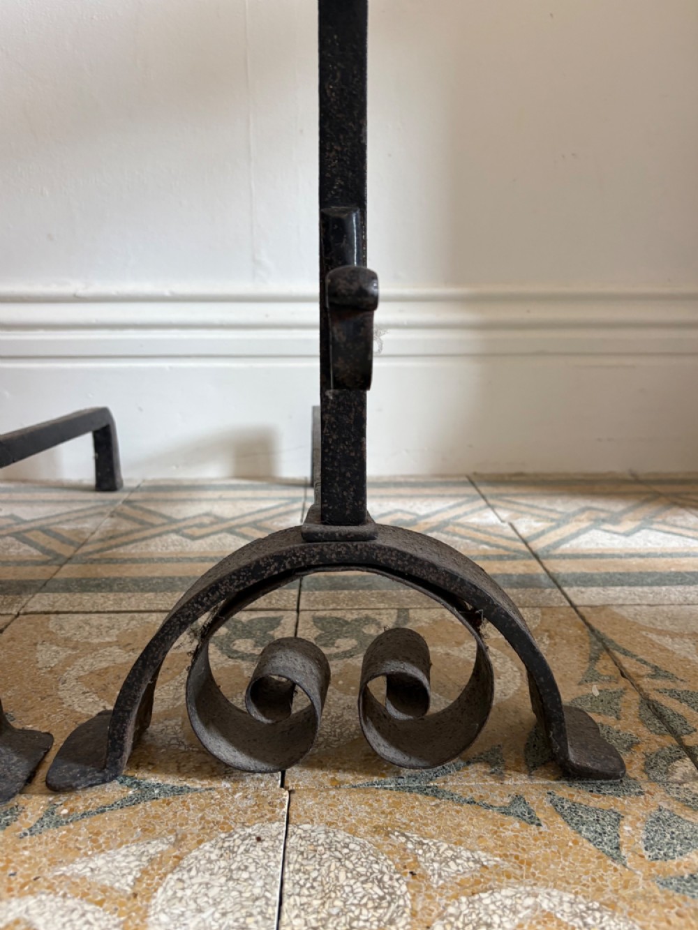 A pair of hand-forged black wrought iron fire dogs featuring circular disc tops, tool hooks, and scrolled arched feet. View IV