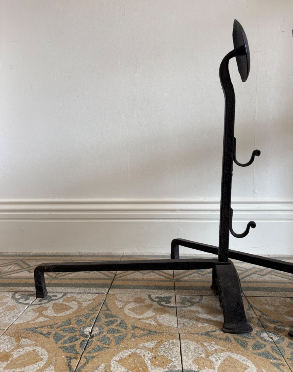 A pair of hand-forged black wrought iron fire dogs featuring circular disc tops, tool hooks, and scrolled arched feet. View VII