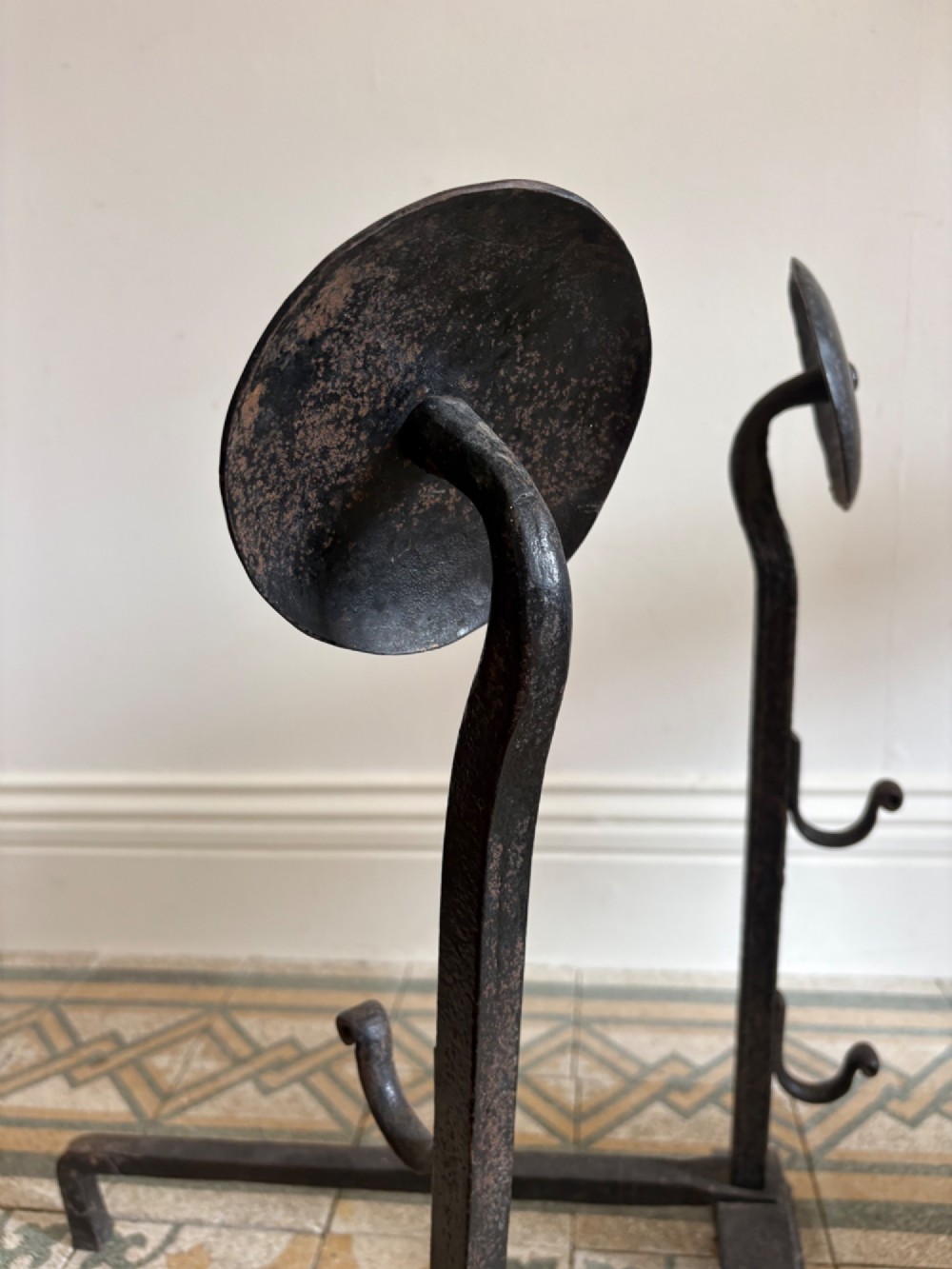 A pair of hand-forged black wrought iron fire dogs featuring circular disc tops, tool hooks, and scrolled arched feet. View IX