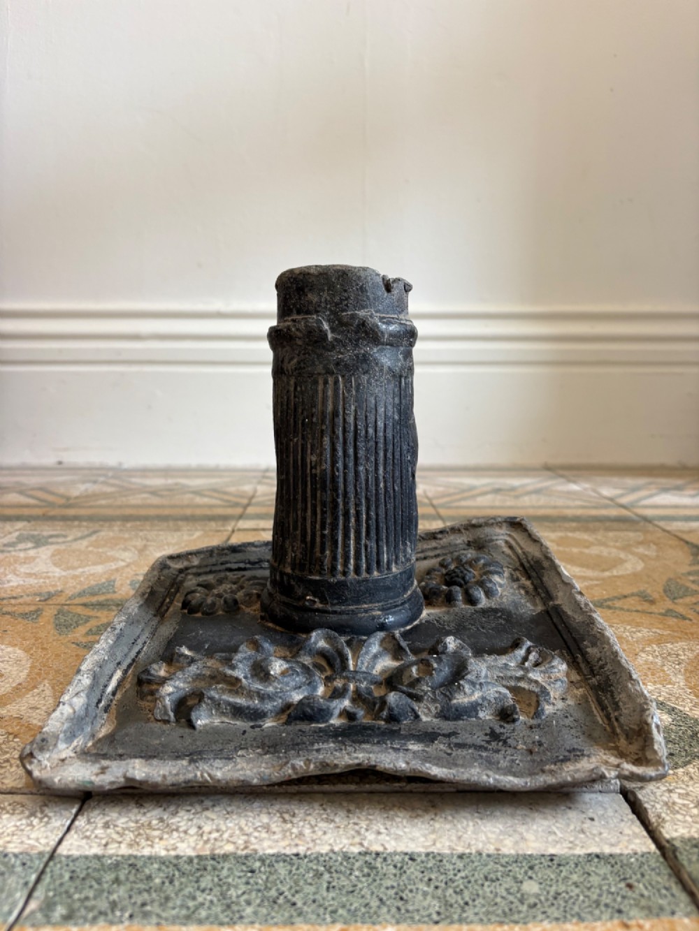 A square dark grey cast lead fountain head featuring a central cylindrical spout above relief-moulded floral rosettes and scrollwork motifs. View IV
