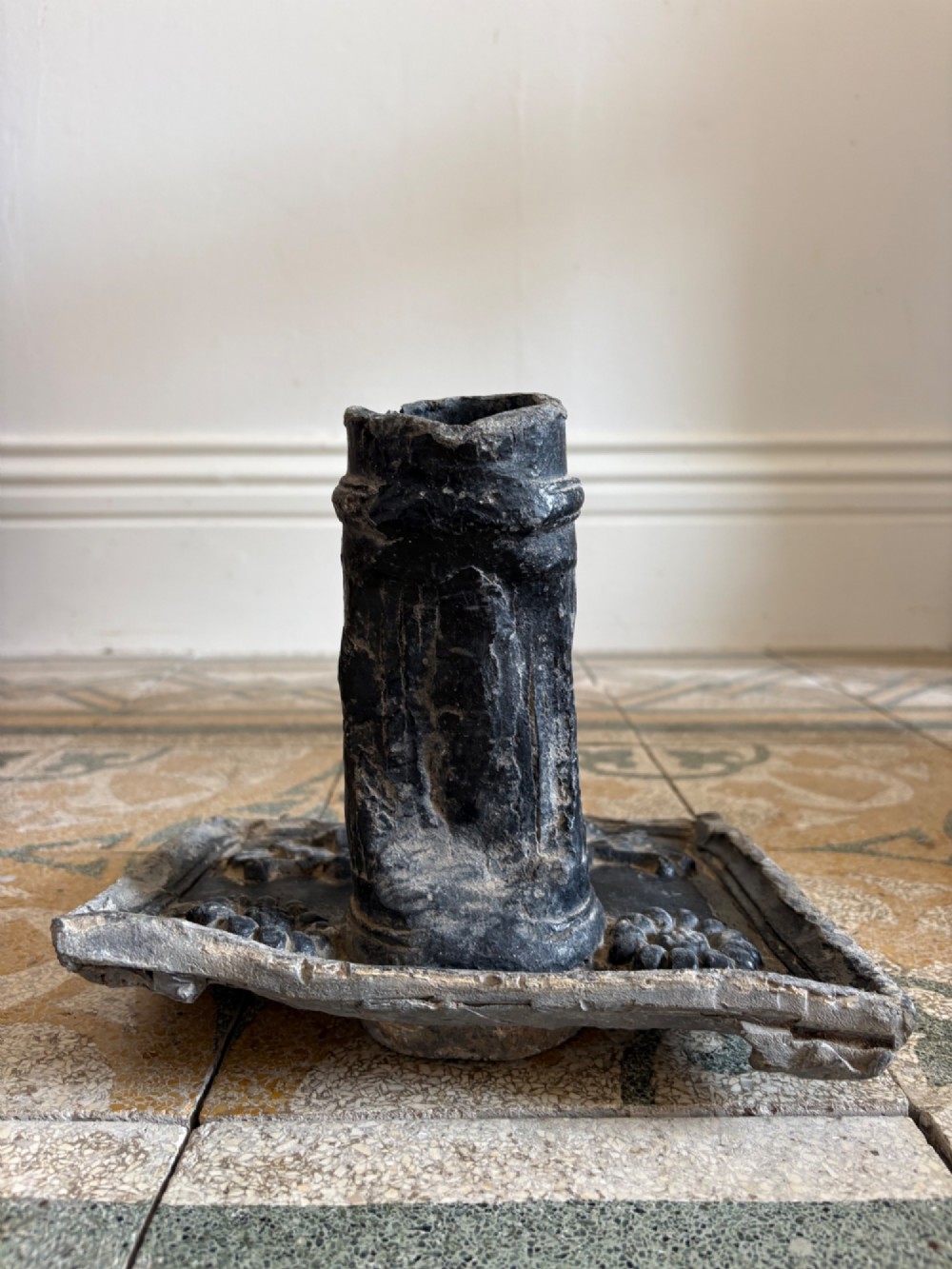 A square dark grey cast lead fountain head featuring a central cylindrical spout above relief-moulded floral rosettes and scrollwork motifs. View VII
