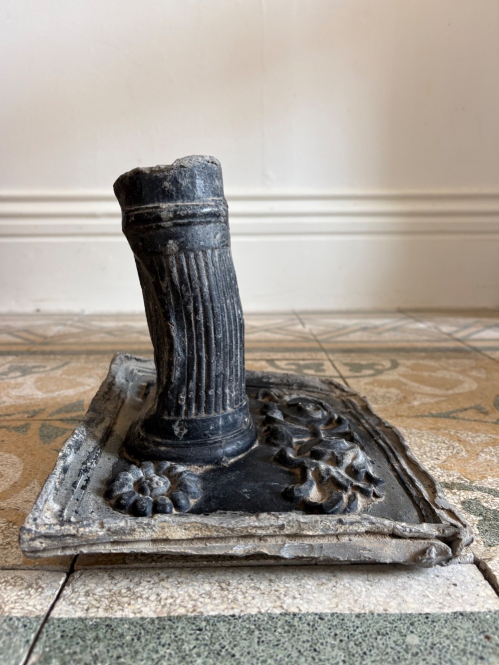 A square dark grey cast lead fountain head featuring a central cylindrical spout above relief-moulded floral rosettes and scrollwork motifs. View VIII