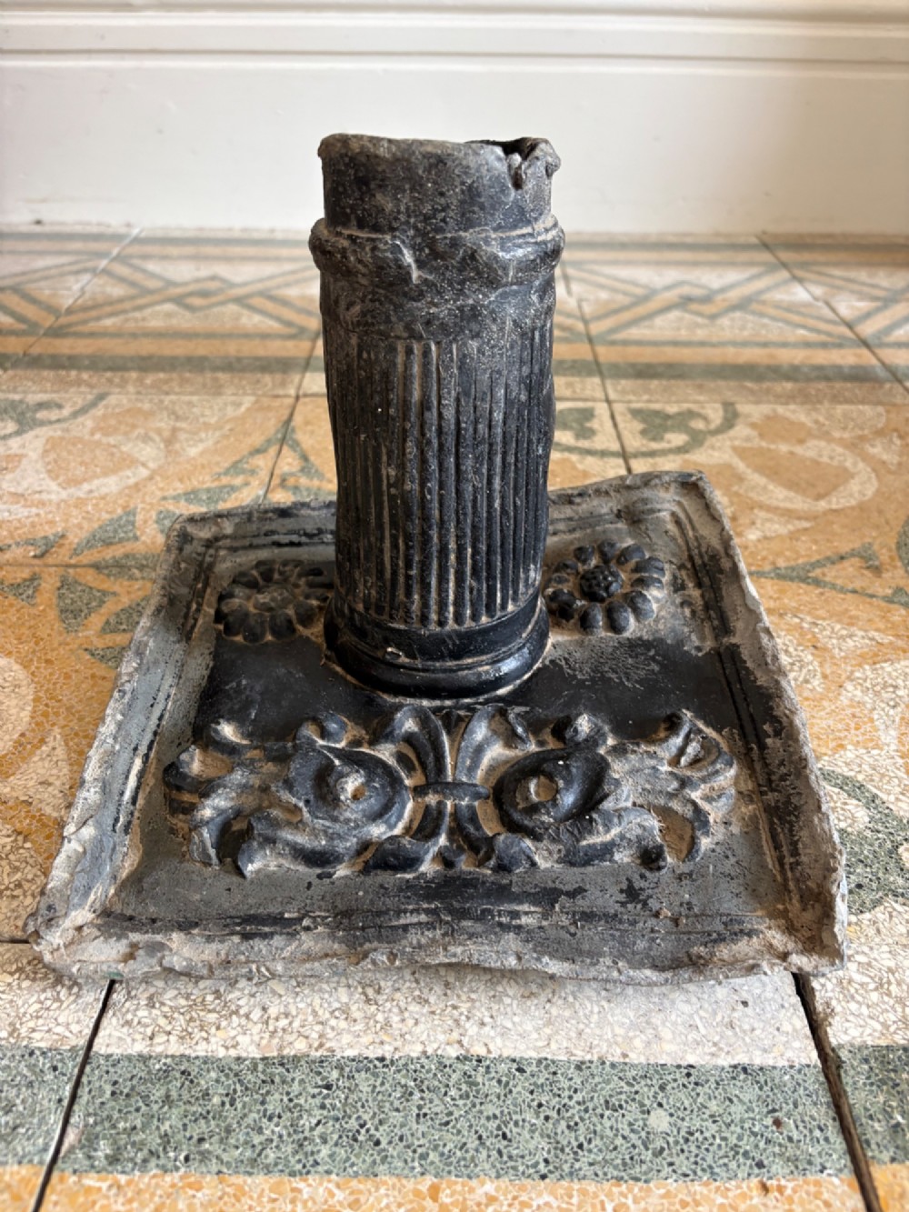 A square dark grey cast lead fountain head featuring a central cylindrical spout above relief-moulded floral rosettes and scrollwork motifs. View XI