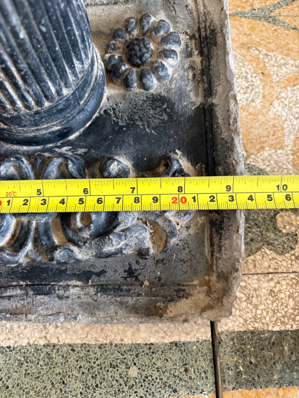 A square dark grey cast lead fountain head featuring a central cylindrical spout above relief-moulded floral rosettes and scrollwork motifs. View XIII