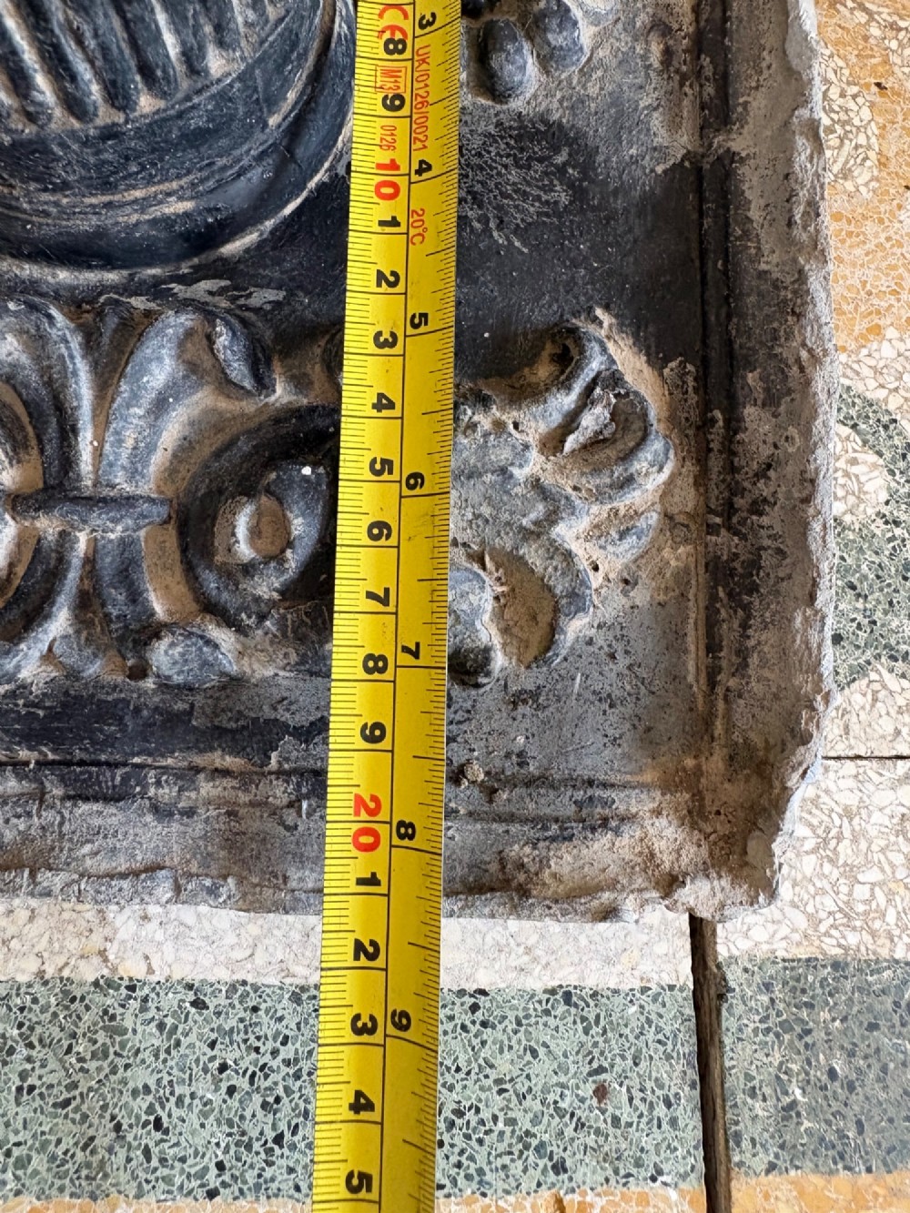 A square dark grey cast lead fountain head featuring a central cylindrical spout above relief-moulded floral rosettes and scrollwork motifs. View XIV