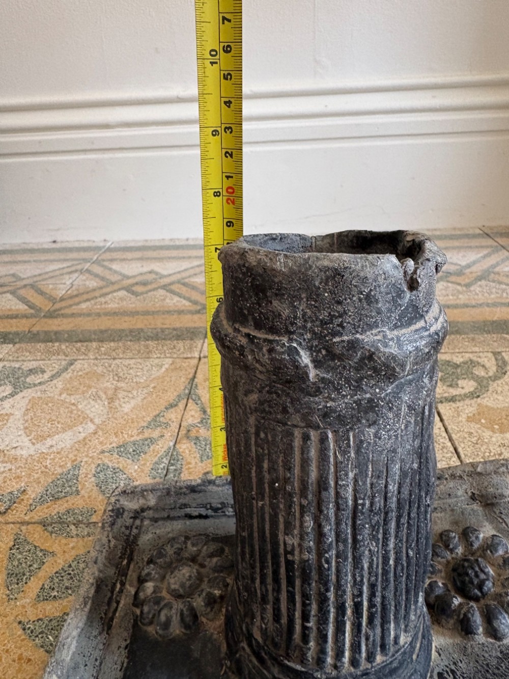 A square dark grey cast lead fountain head featuring a central cylindrical spout above relief-moulded floral rosettes and scrollwork motifs. View XV