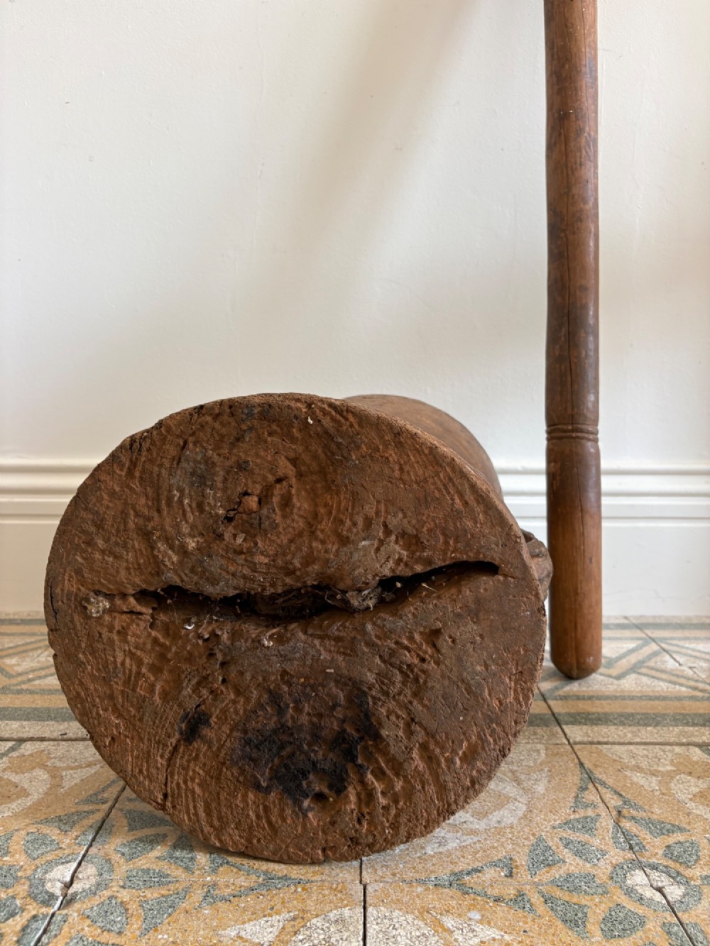 A hand-carved African hardwood grain mortar with side loop handles and concentric carved grooves, next to a tall wooden pestle pole. View IV