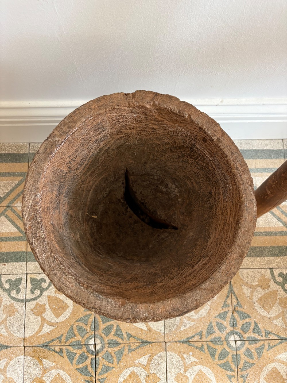A hand-carved African hardwood grain mortar with side loop handles and concentric carved grooves, next to a tall wooden pestle pole. View VI