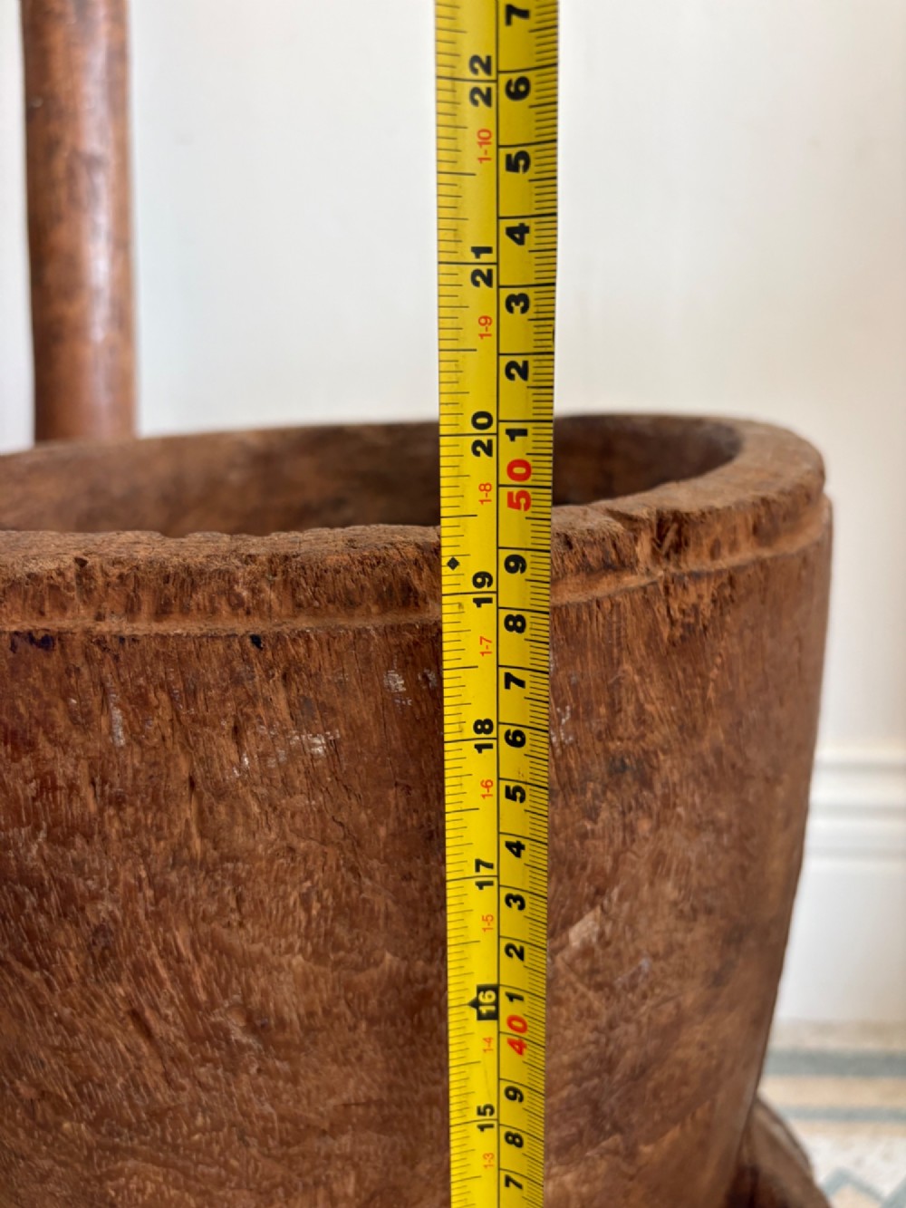 A hand-carved African hardwood grain mortar with side loop handles and concentric carved grooves, next to a tall wooden pestle pole. View XII