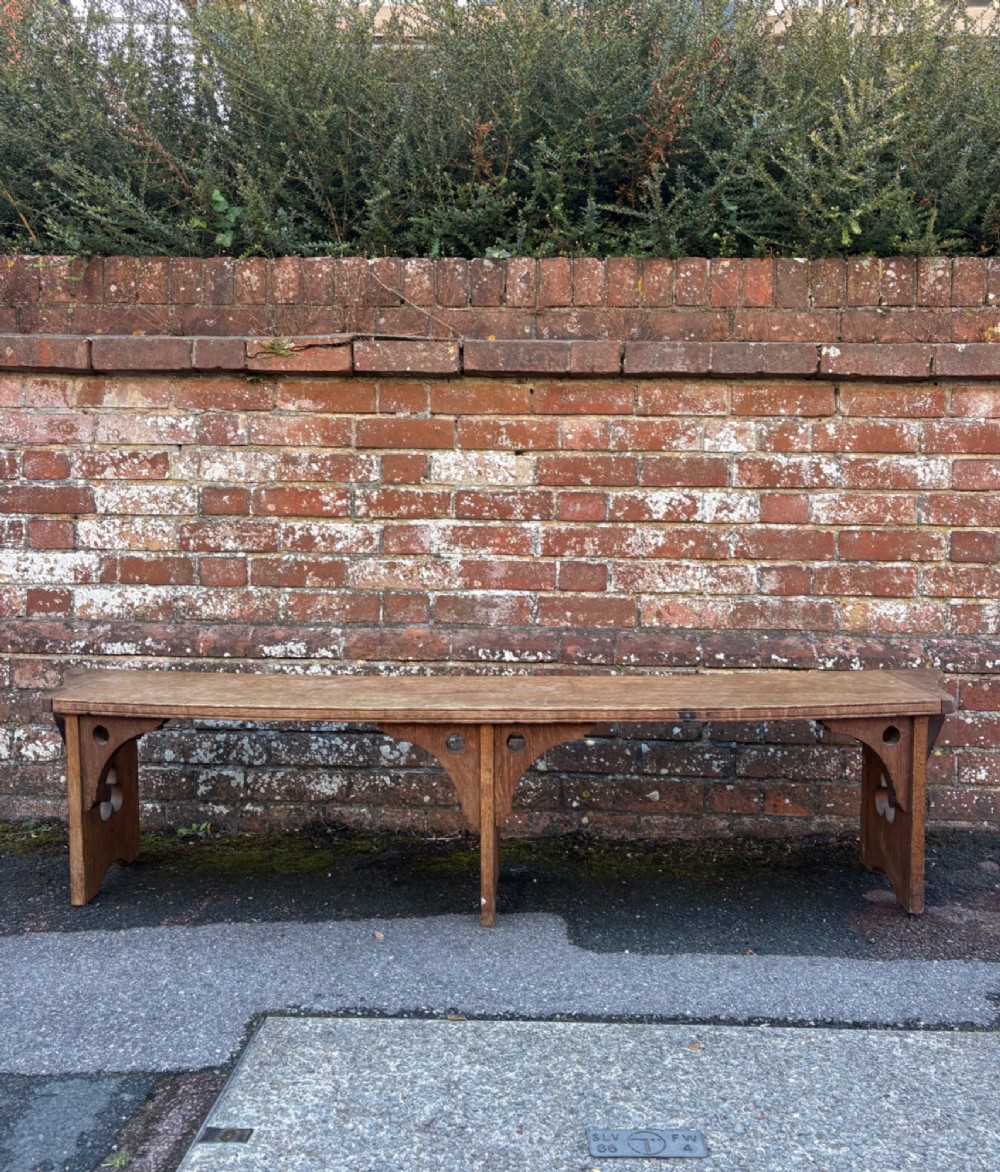 A long curved oak bench featuring trefoil carved cut-outs on the end supports. View II