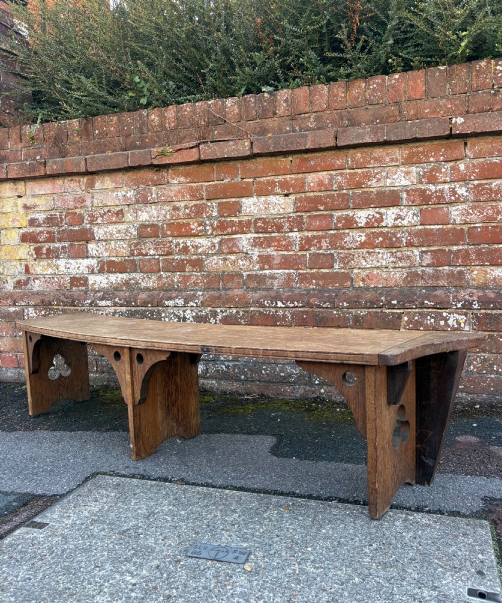 A long curved oak bench featuring trefoil carved cut-outs on the end supports.
