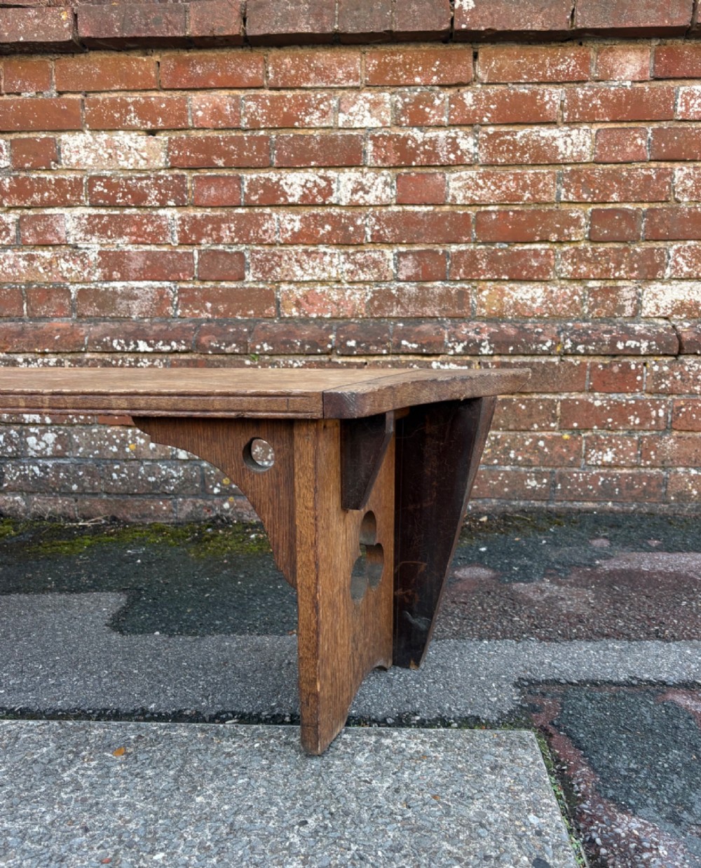 A long curved oak bench featuring trefoil carved cut-outs on the end supports. View IX