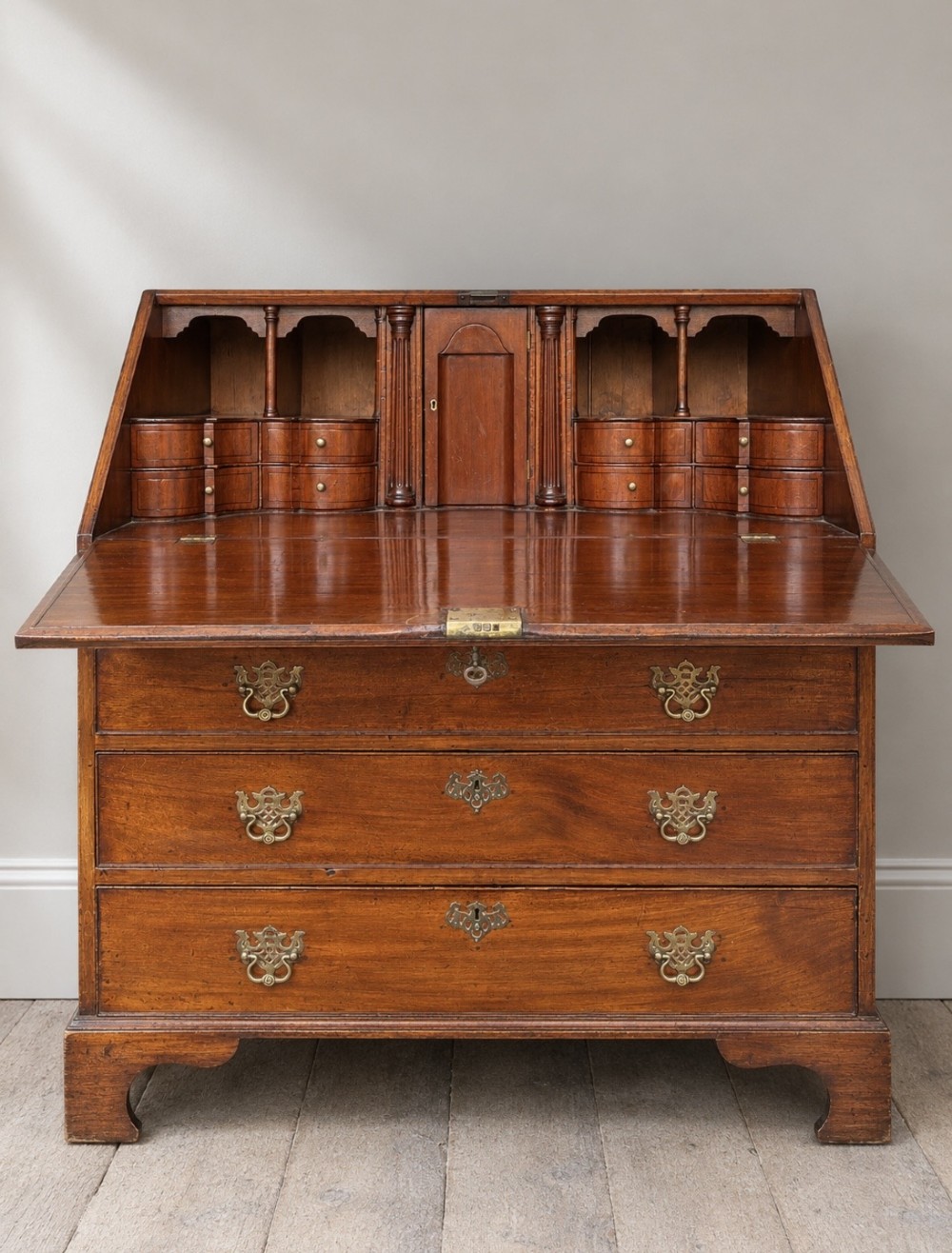 An 18th-century Georgian mahogany slant-front bureau shown open, featuring a fitted interior with small drawers and pigeonholes above three long drawers with brass handles, resting on bracket feet.
