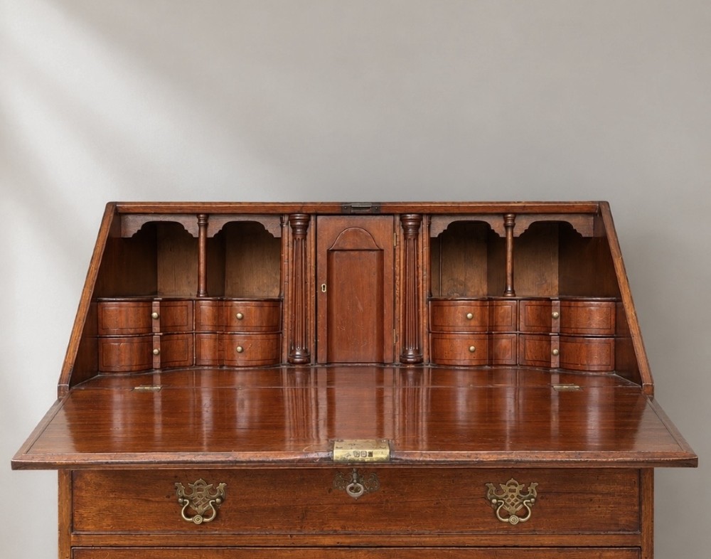 An 18th-century Georgian mahogany slant-front bureau shown open, featuring a fitted interior with small drawers and pigeonholes above three long drawers with brass handles, resting on bracket feet. View IV