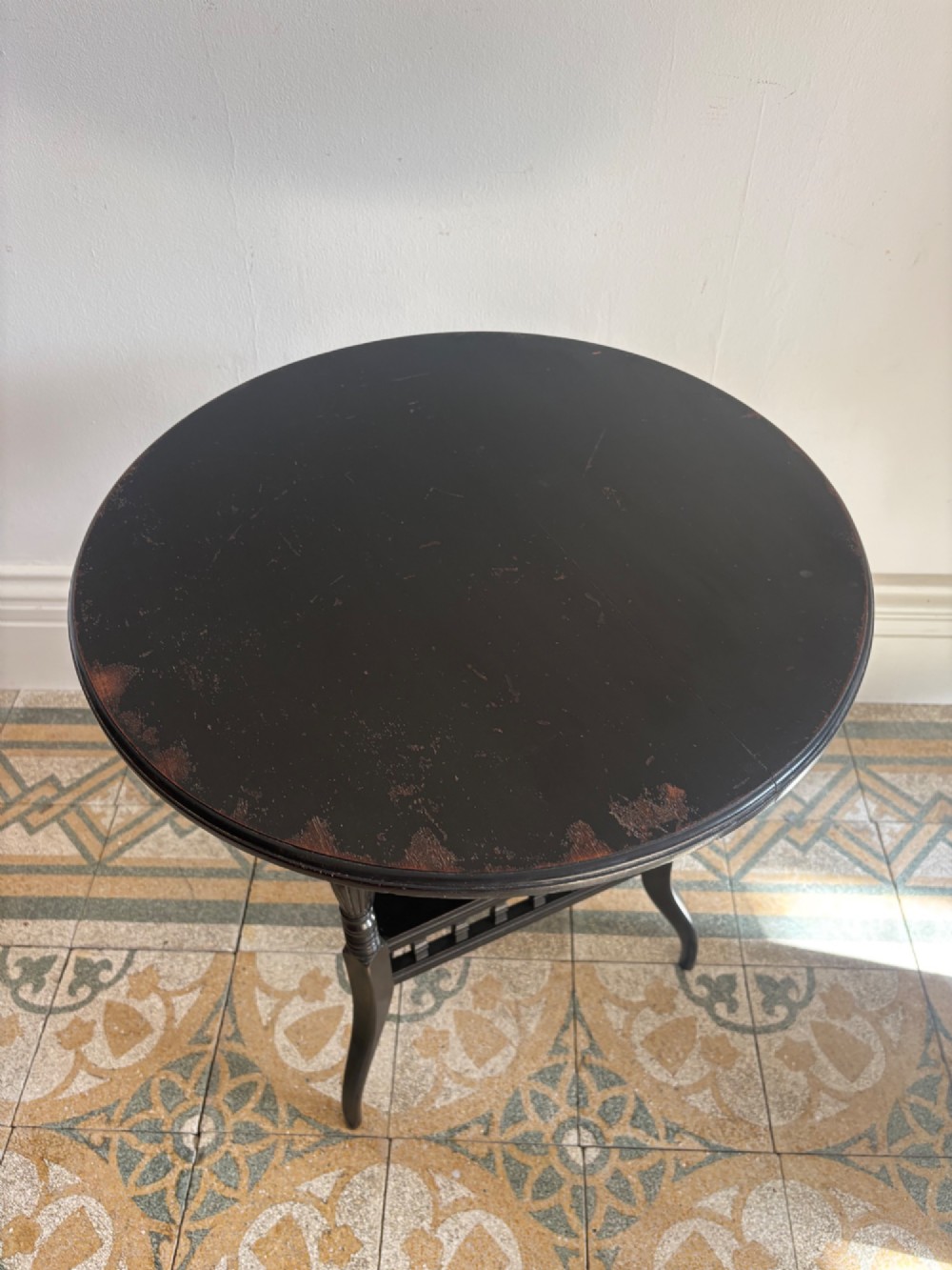 A late 19th-century ebonised round side table featuring three turned legs, slender splayed feet, and a lower triangular shelf bounded by a spindled gallery. View VIII