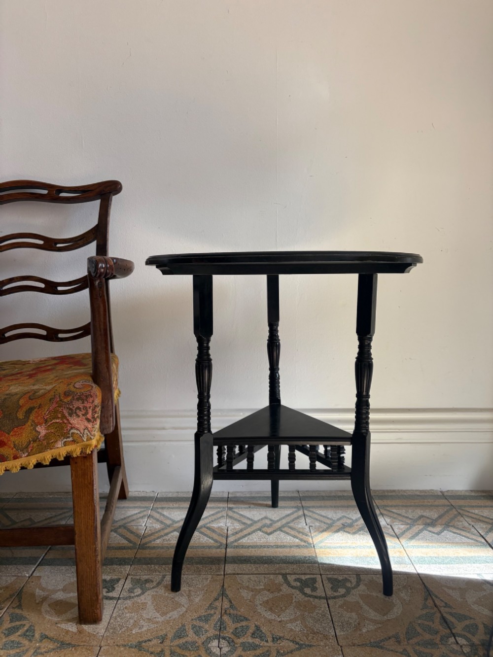 A late 19th-century ebonised round side table featuring three turned legs, slender splayed feet, and a lower triangular shelf bounded by a spindled gallery. View IX