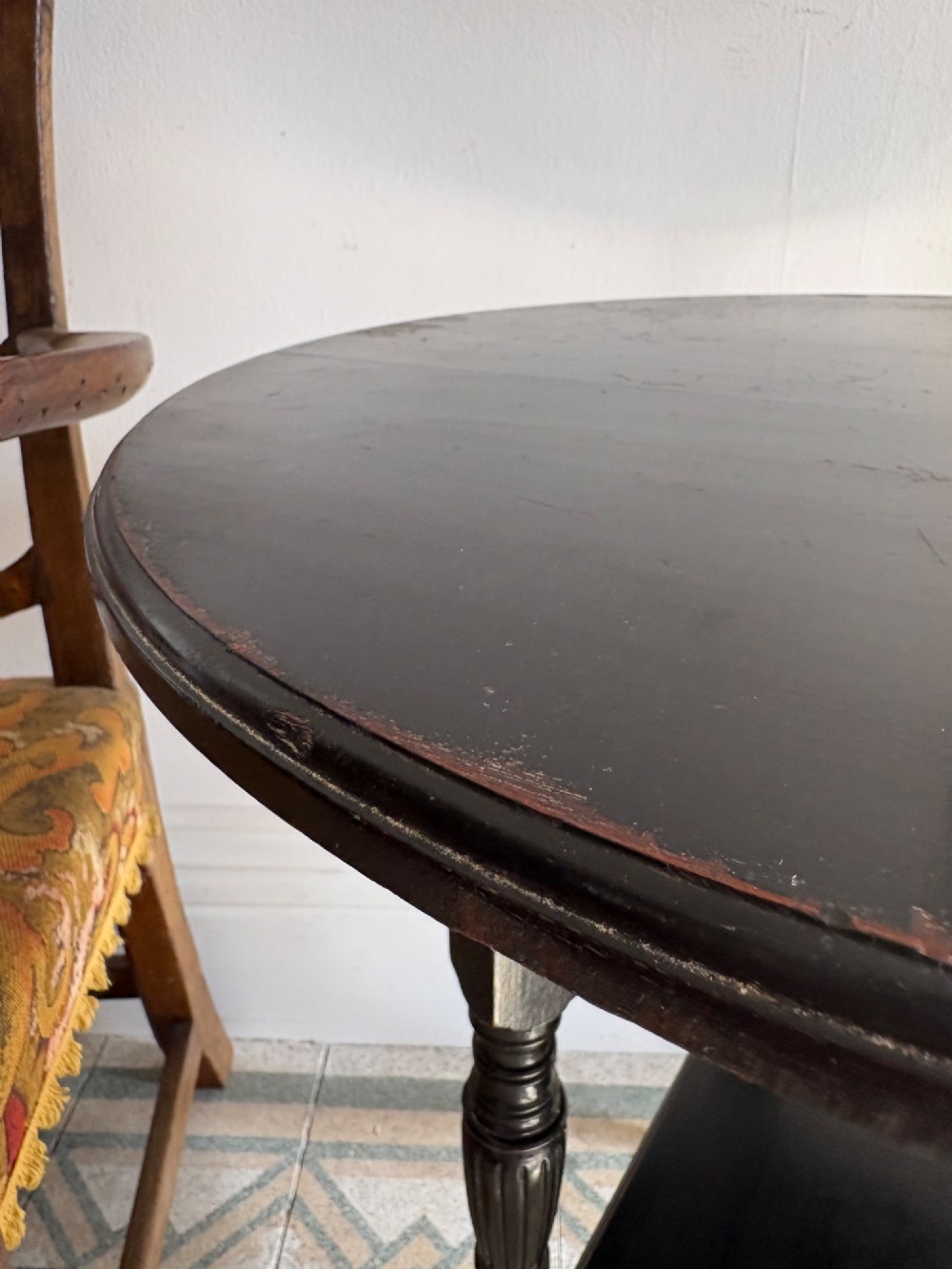 A late 19th-century ebonised round side table featuring three turned legs, slender splayed feet, and a lower triangular shelf bounded by a spindled gallery. View XI