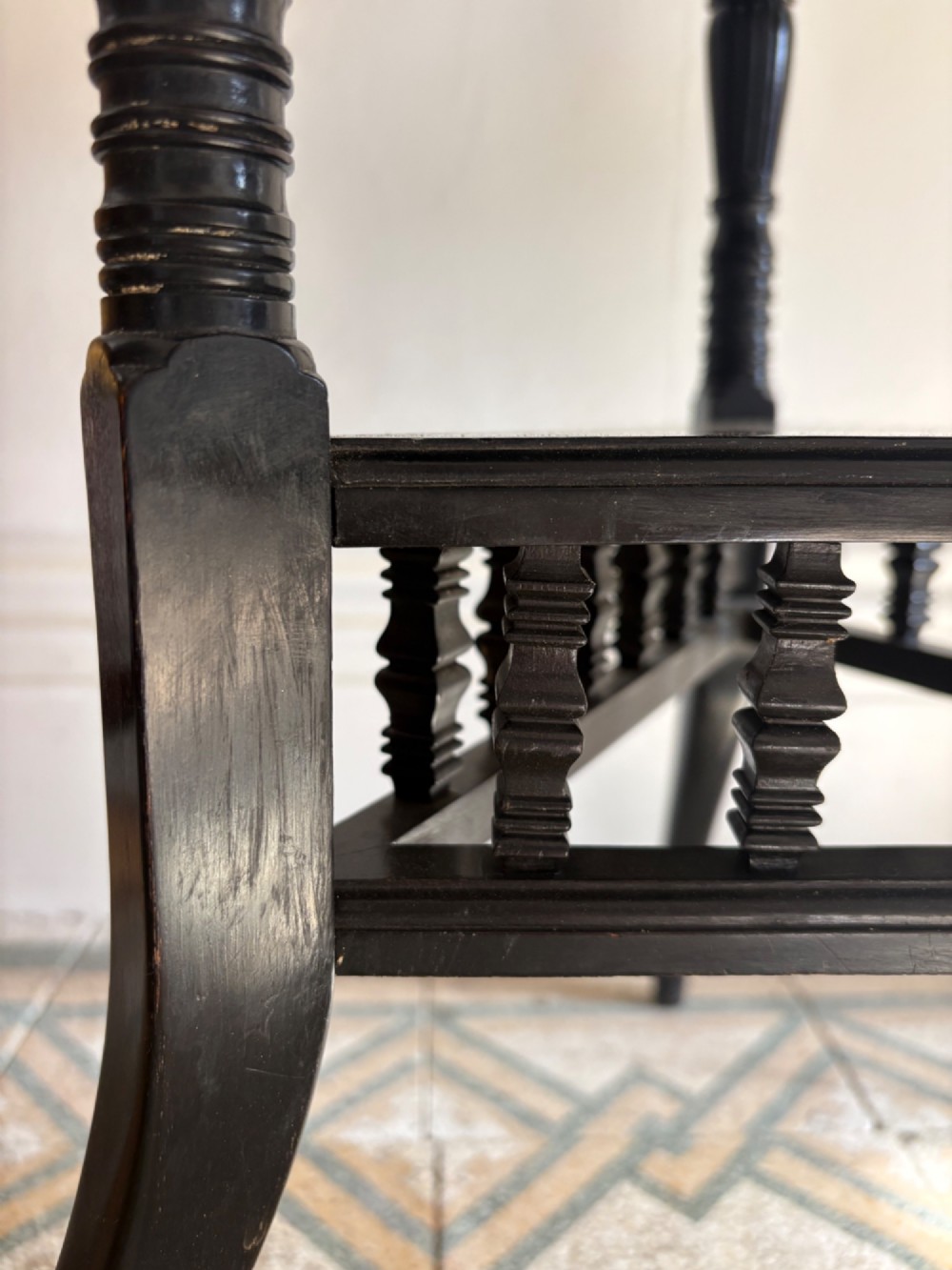 A late 19th-century ebonised round side table featuring three turned legs, slender splayed feet, and a lower triangular shelf bounded by a spindled gallery. View XII