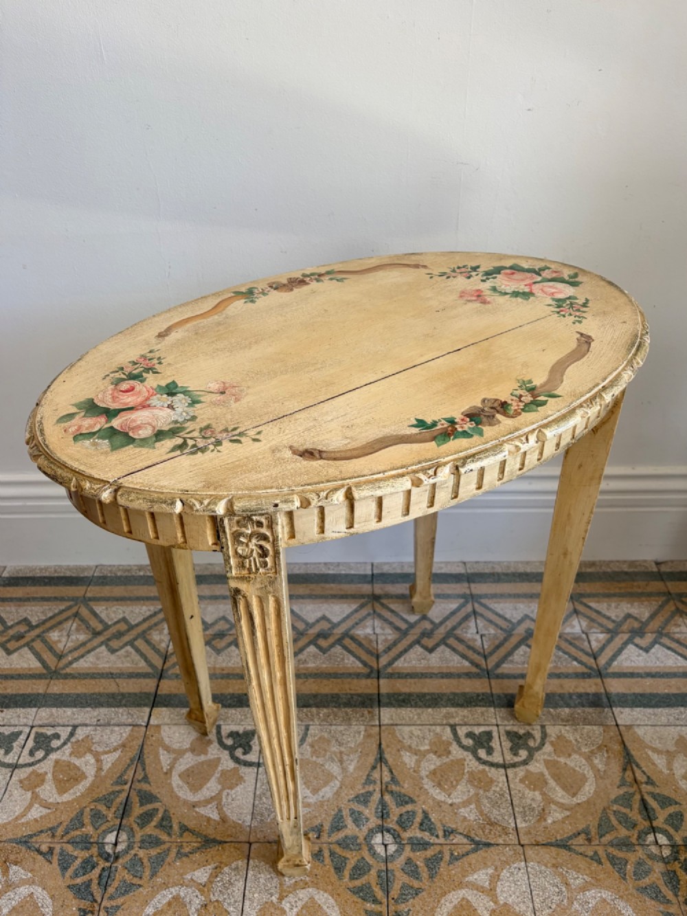 An oval cream-painted mahogany occasional table with hand-painted floral garlands, fluted apron, and square tapered fluted legs.