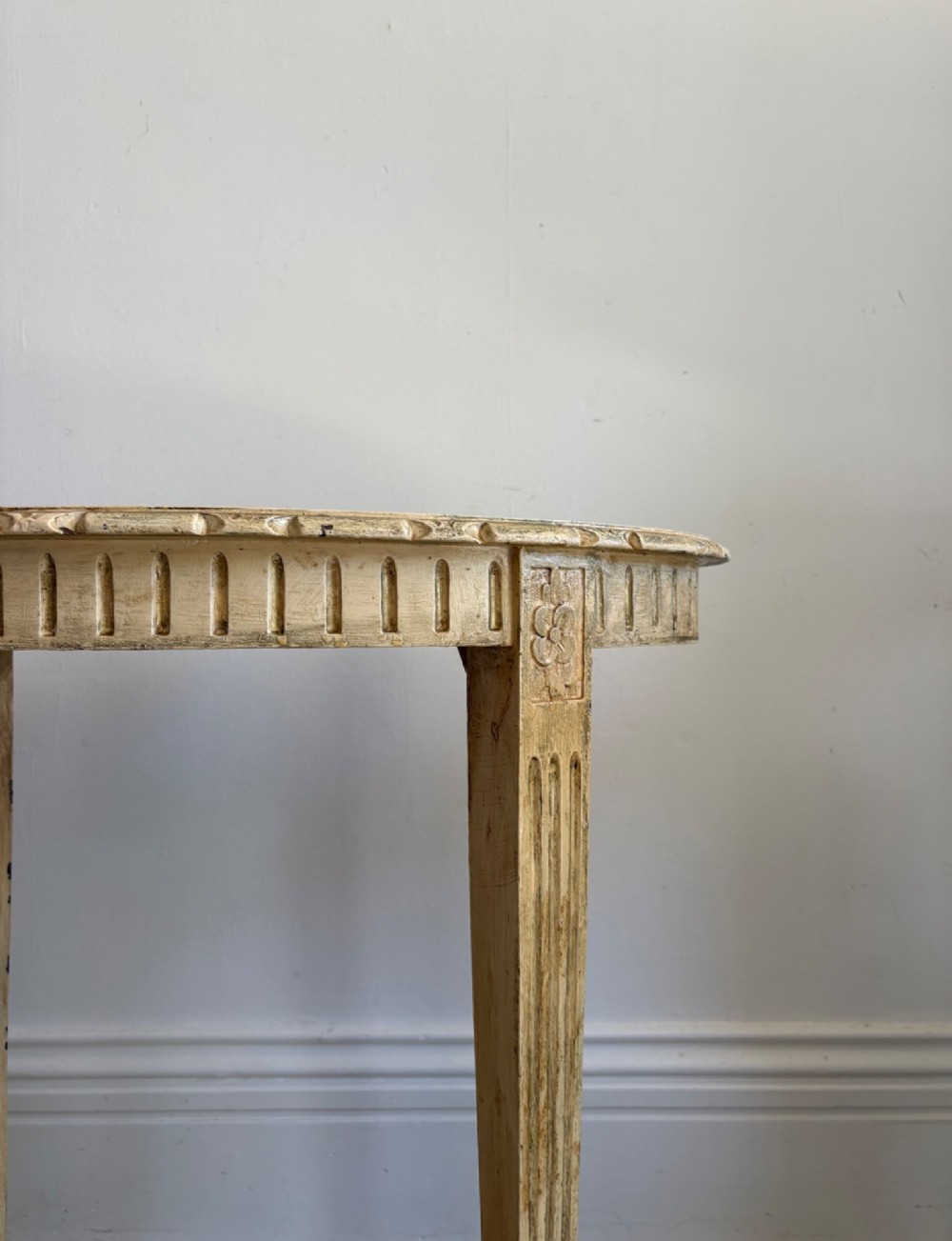 An oval cream-painted mahogany occasional table with hand-painted floral garlands, fluted apron, and square tapered fluted legs. View V