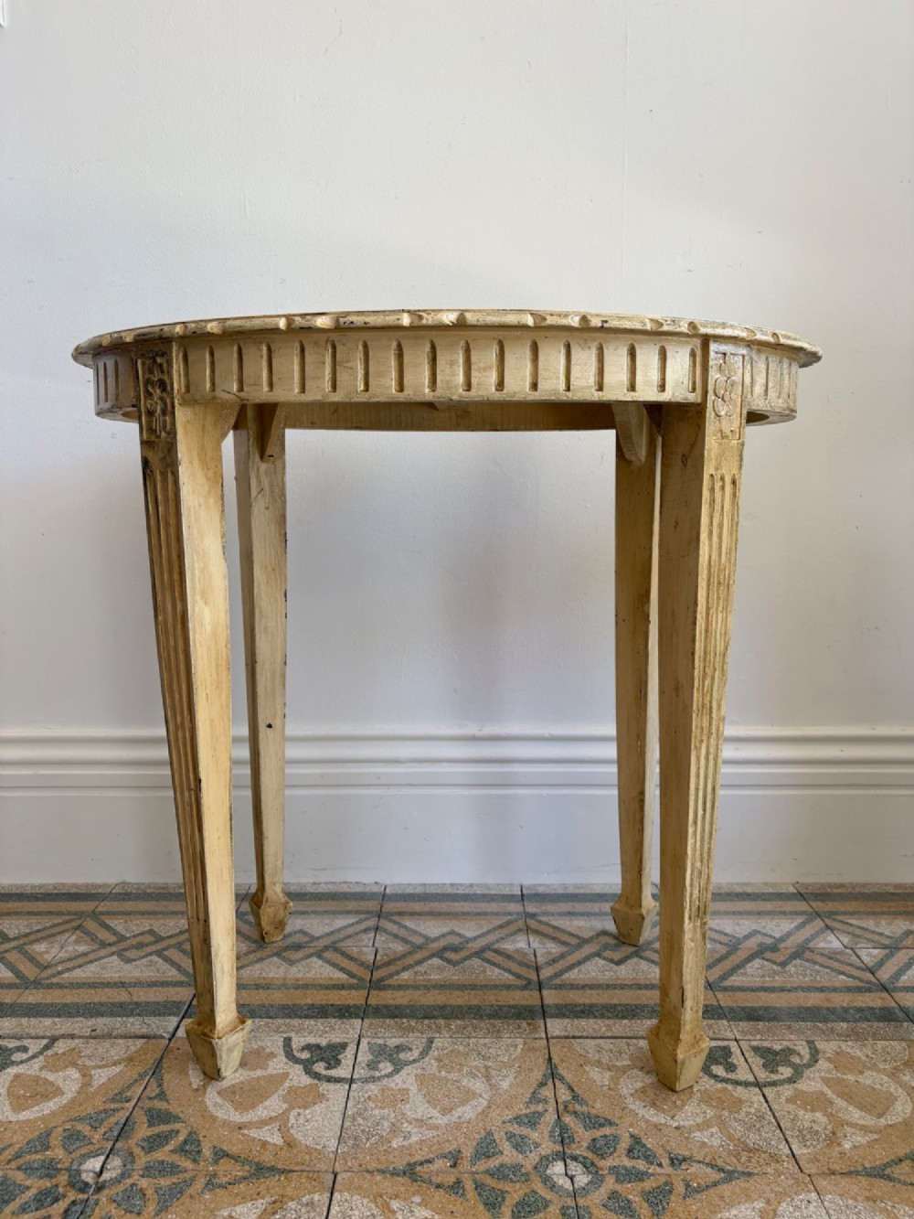 An oval cream-painted mahogany occasional table with hand-painted floral garlands, fluted apron, and square tapered fluted legs. View VII