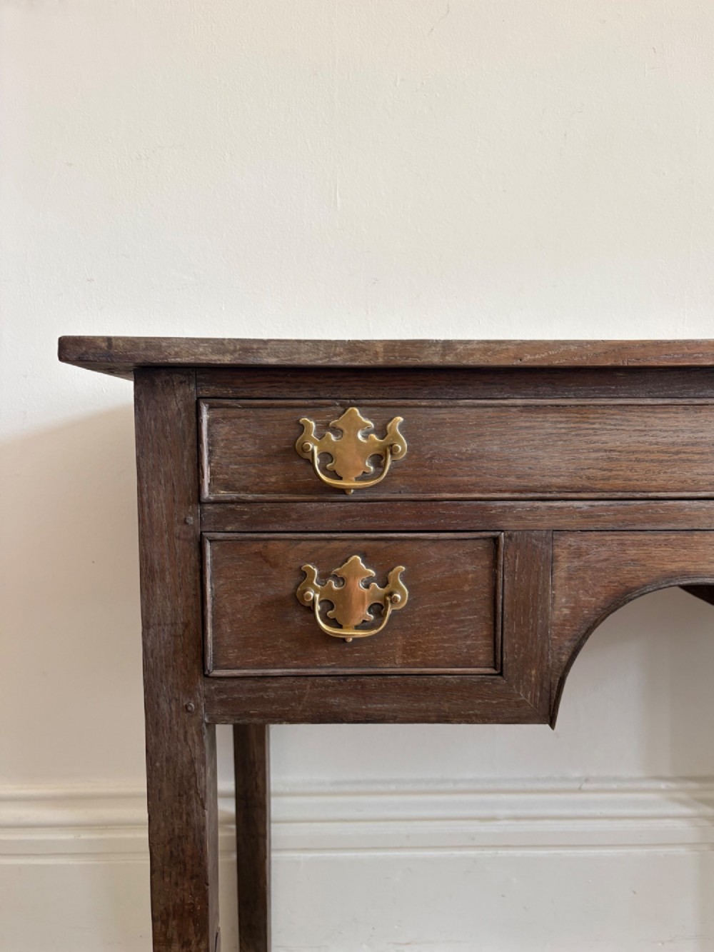 An early eighteenth-century oak lowboy side table featuring one wide upper drawer, two small side drawers, an arched apron, brass handles, and straight square legs. View II