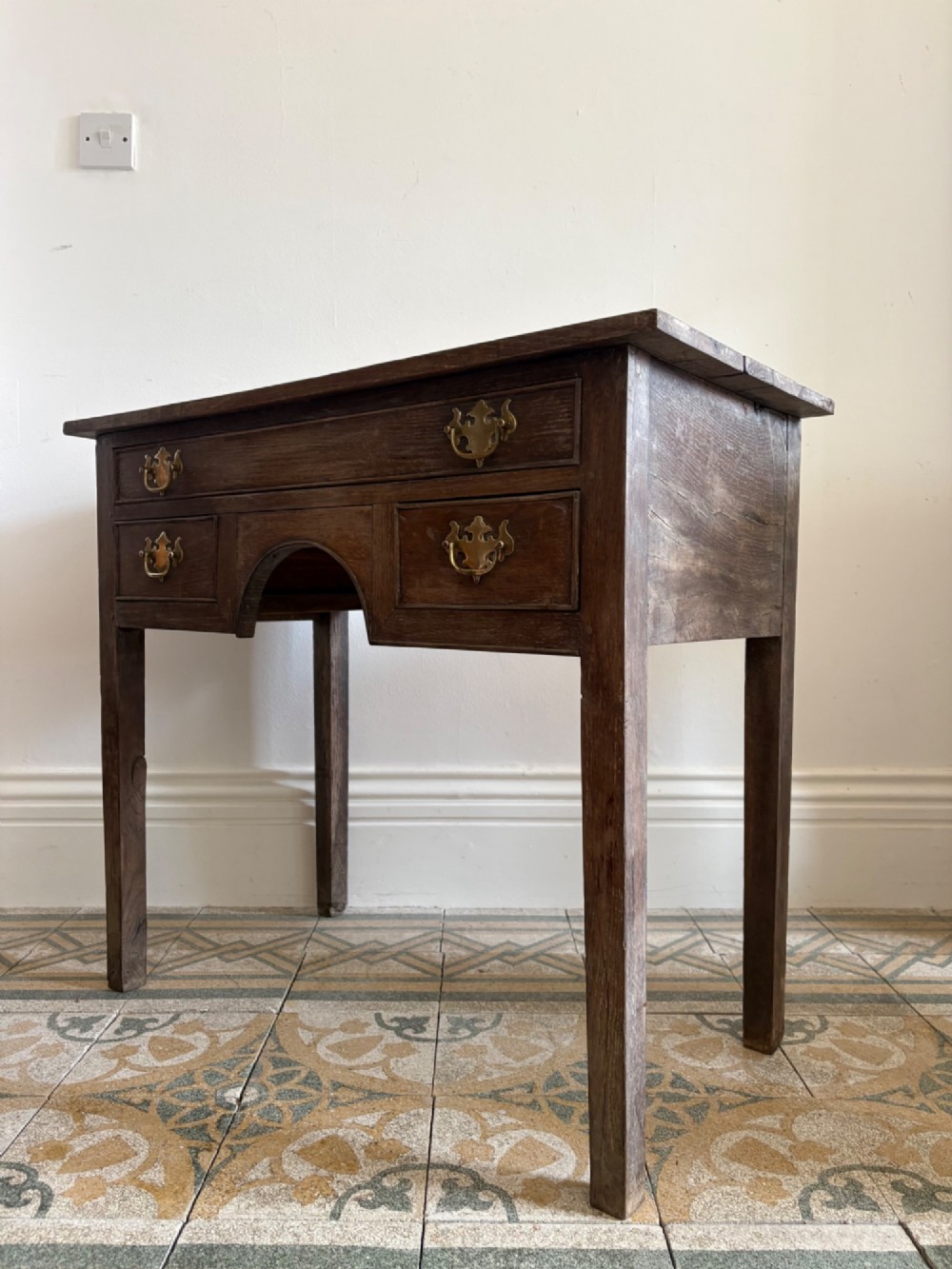 An early eighteenth-century oak lowboy side table featuring one wide upper drawer, two small side drawers, an arched apron, brass handles, and straight square legs. View III