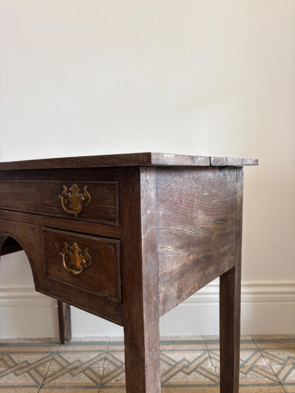 An early eighteenth-century oak lowboy side table featuring one wide upper drawer, two small side drawers, an arched apron, brass handles, and straight square legs. View IV