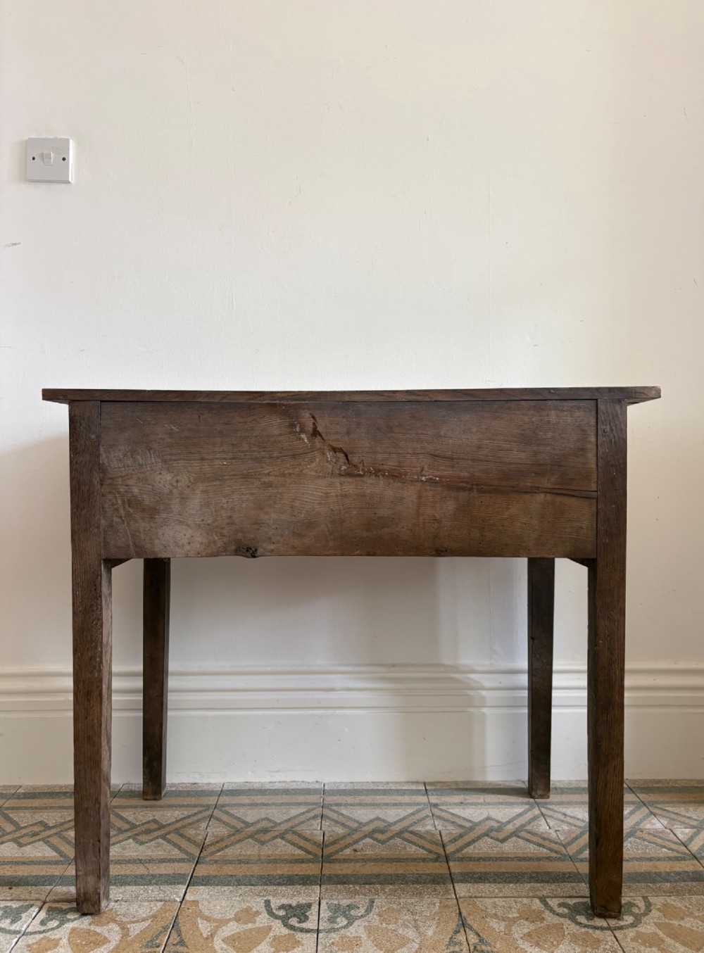 An early eighteenth-century oak lowboy side table featuring one wide upper drawer, two small side drawers, an arched apron, brass handles, and straight square legs. View V