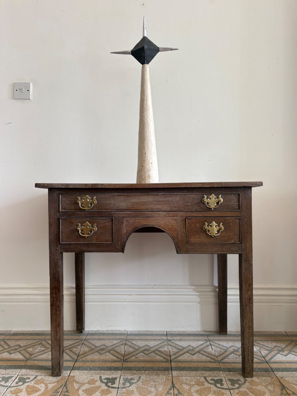 An early eighteenth-century oak lowboy side table featuring one wide upper drawer, two small side drawers, an arched apron, brass handles, and straight square legs. View VI