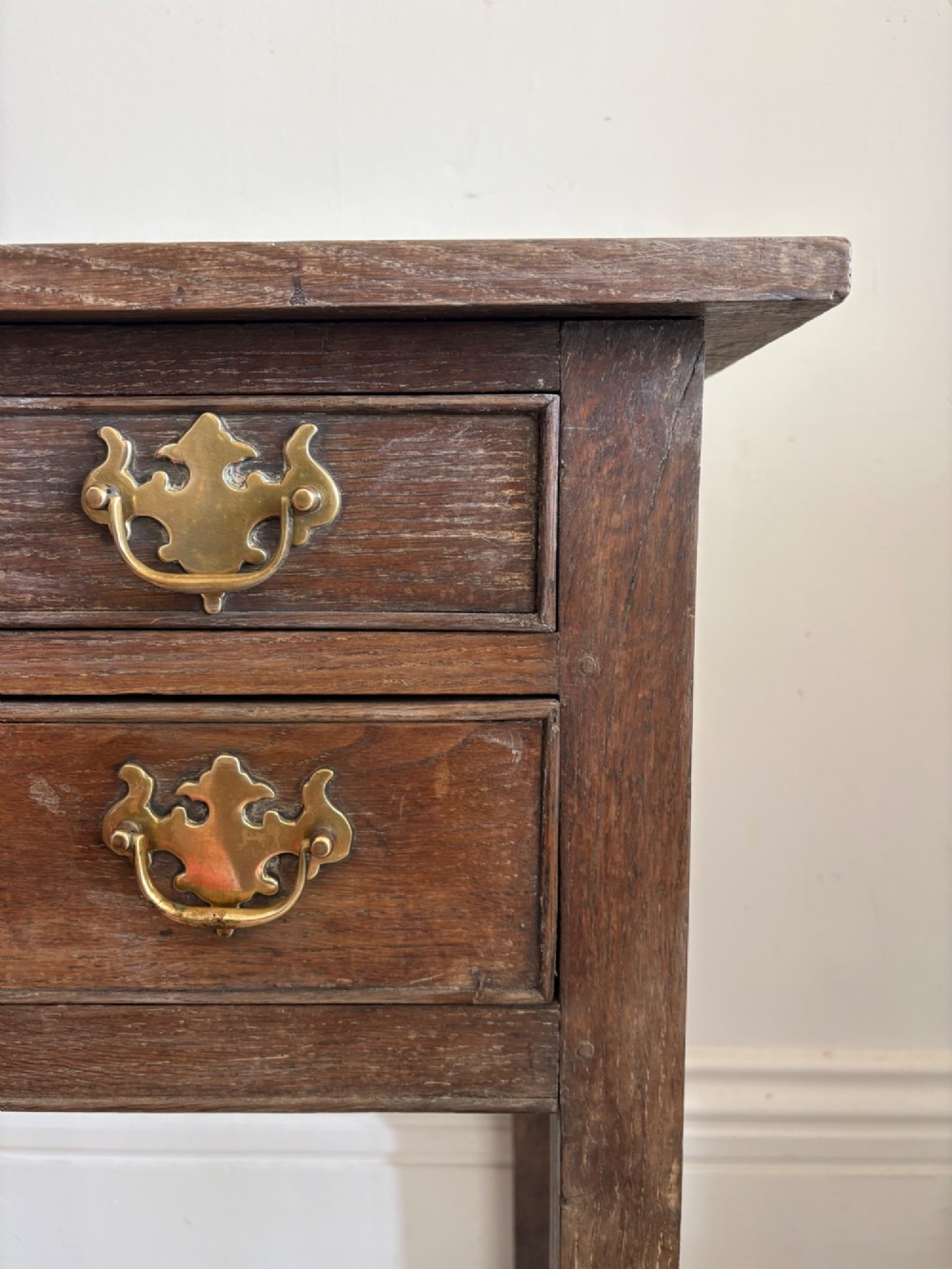 An early eighteenth-century oak lowboy side table featuring one wide upper drawer, two small side drawers, an arched apron, brass handles, and straight square legs. View IX