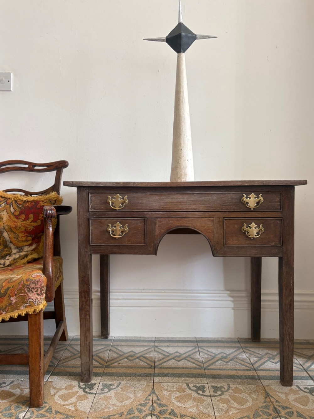 An early eighteenth-century oak lowboy side table featuring one wide upper drawer, two small side drawers, an arched apron, brass handles, and straight square legs. View X
