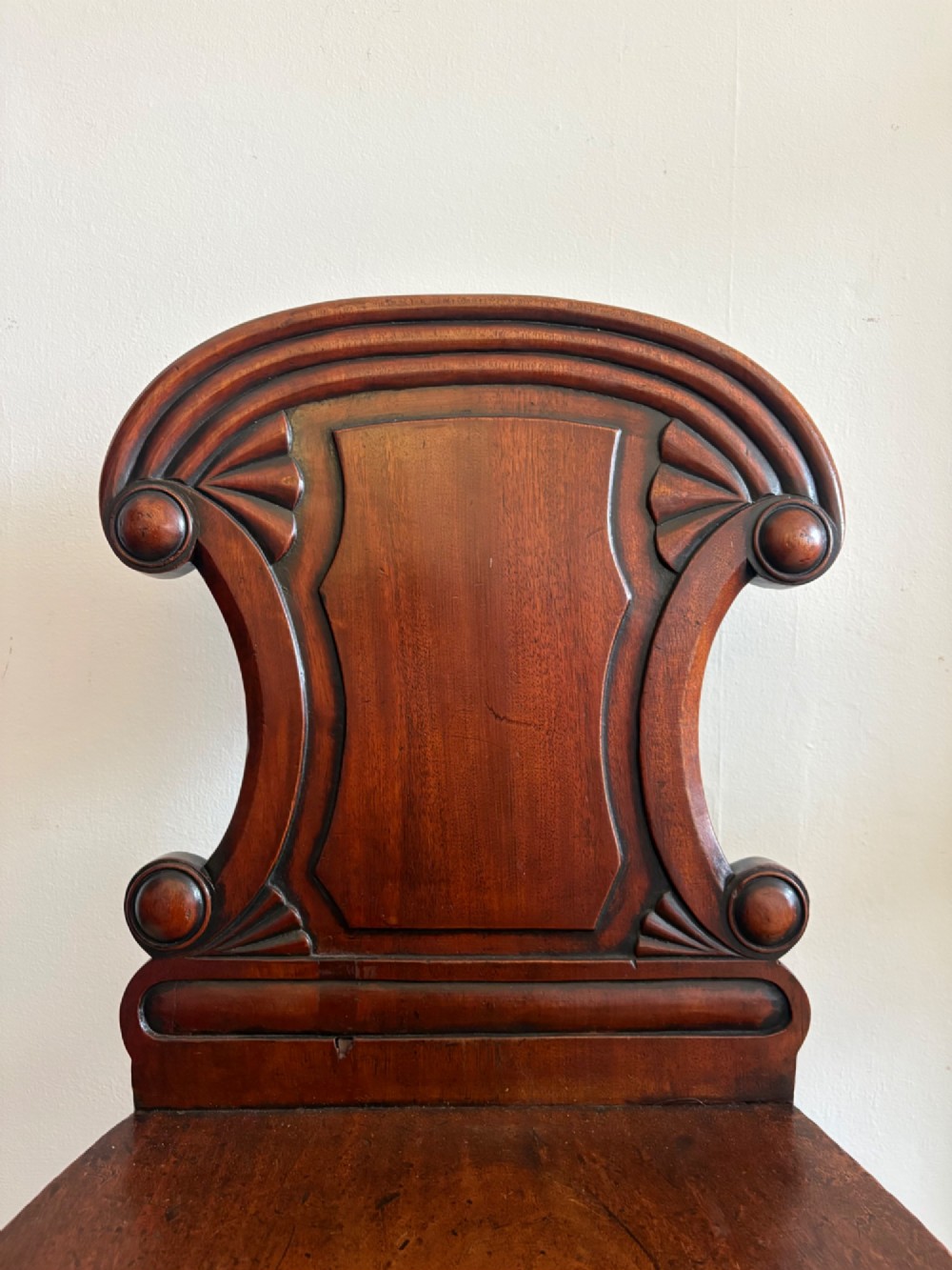 An antique William IV mahogany hall chair featuring a carved crest backrest, solid flat seat, and fluted turned front legs. View III