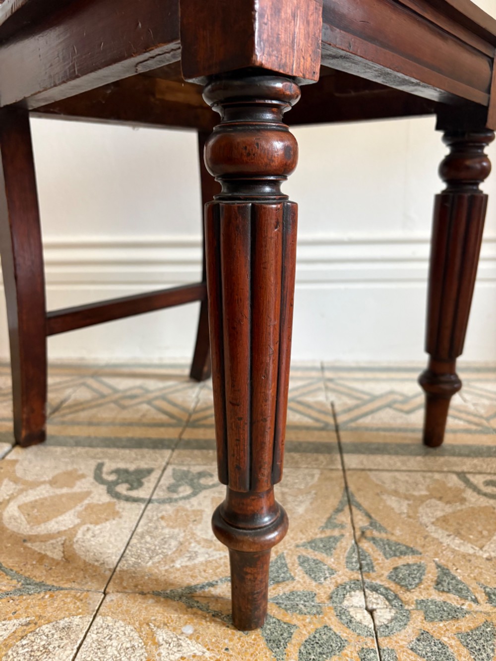 An antique William IV mahogany hall chair featuring a carved crest backrest, solid flat seat, and fluted turned front legs. View VII