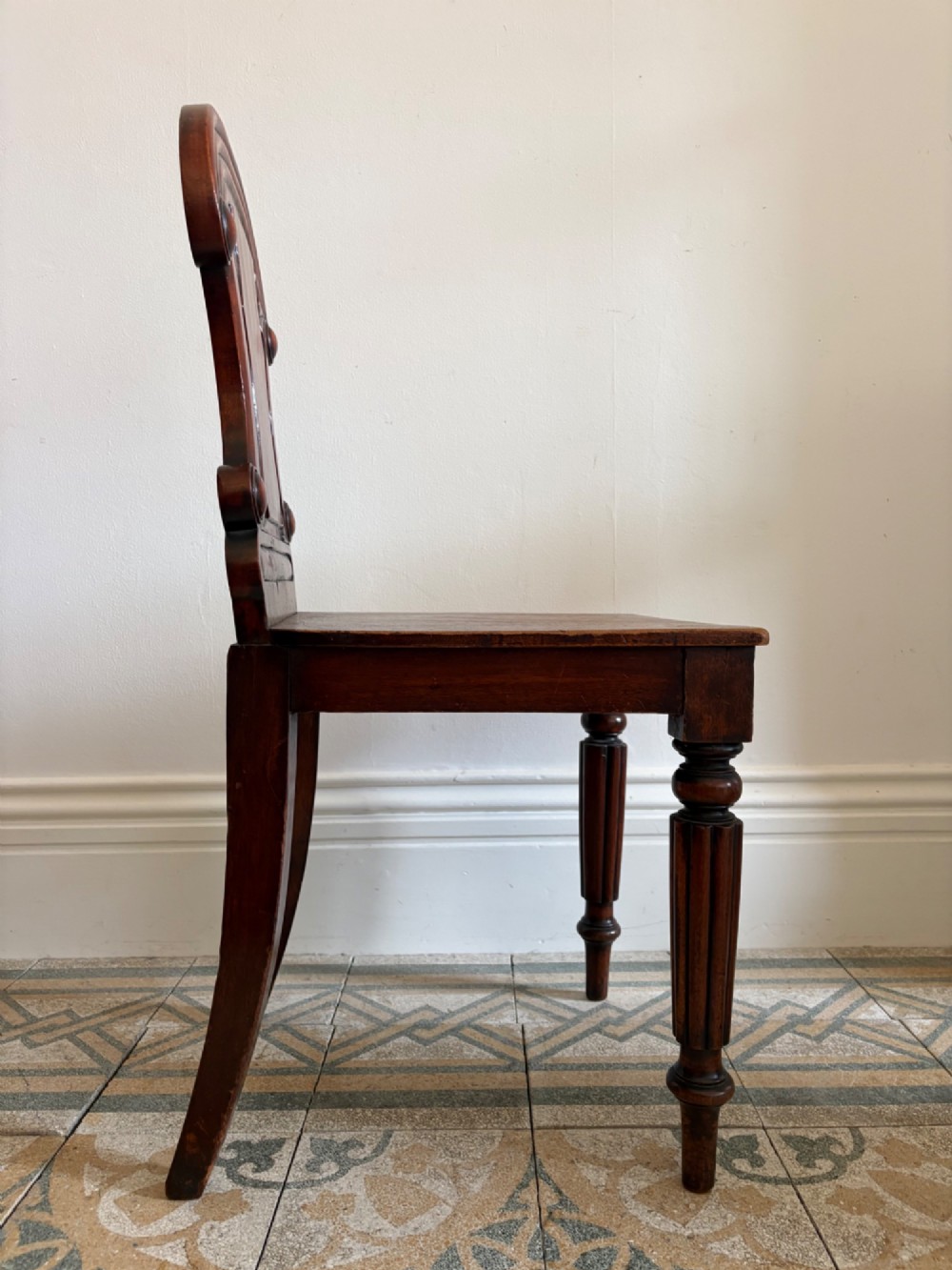 An antique William IV mahogany hall chair featuring a carved crest backrest, solid flat seat, and fluted turned front legs. View VIII