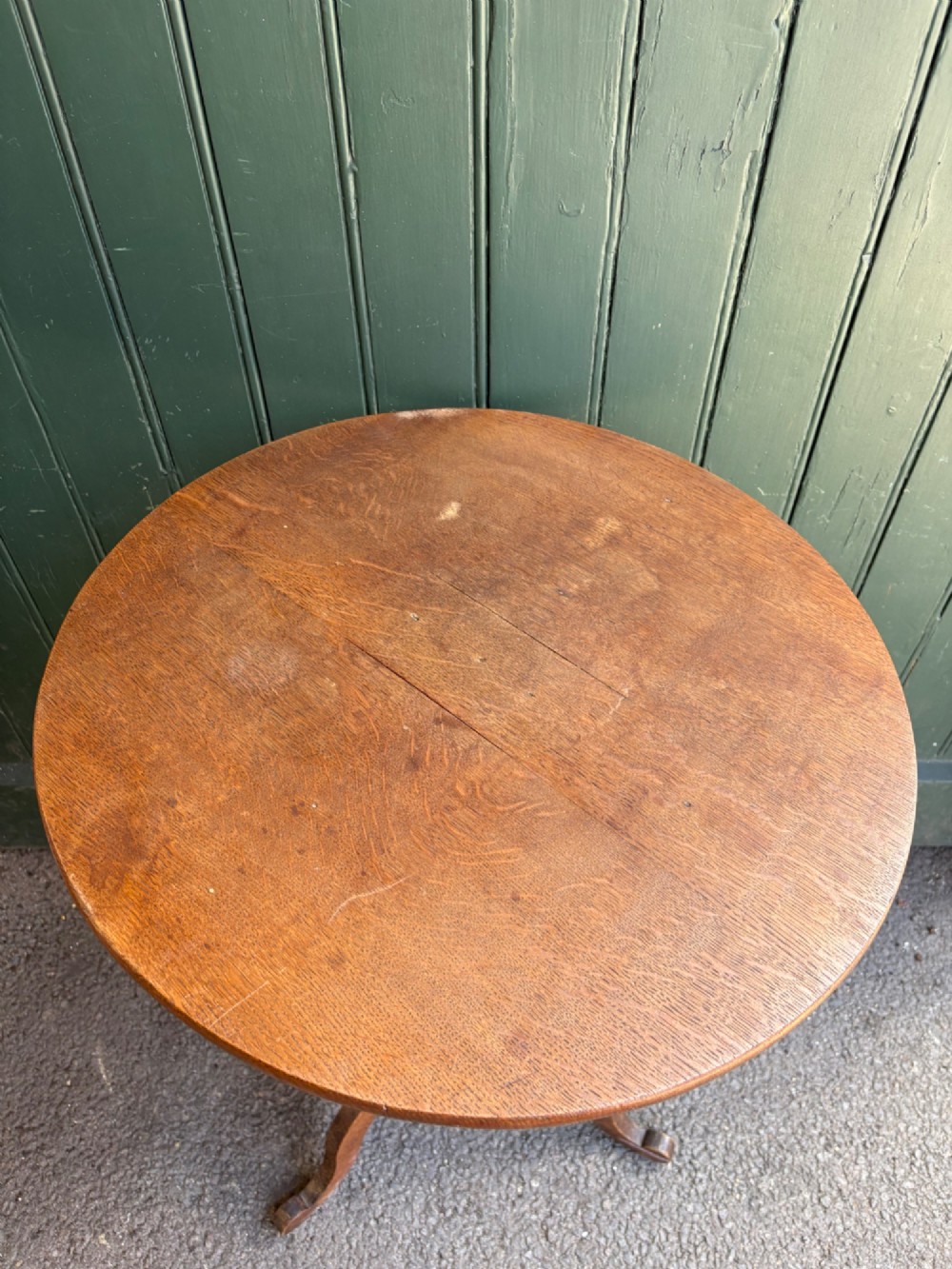 An English Arts and Crafts solid oak wine table featuring a circular top, an under-top support bracket, a central column terminating in a pointed lower finial, and three splayed cabriole legs. View VII