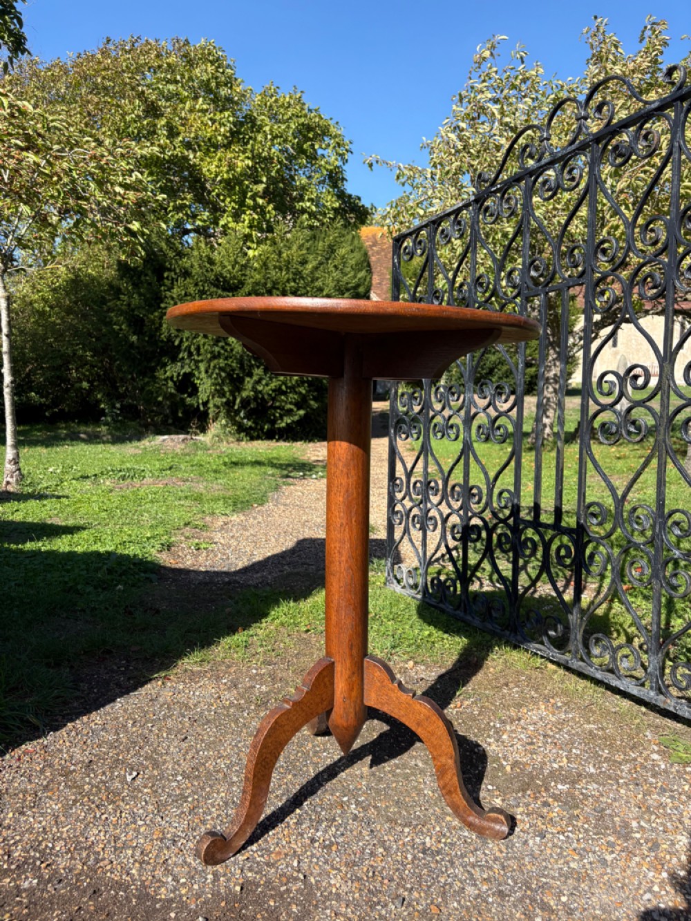An English Arts and Crafts solid oak wine table featuring a circular top, an under-top support bracket, a central column terminating in a pointed lower finial, and three splayed cabriole legs. View VIII