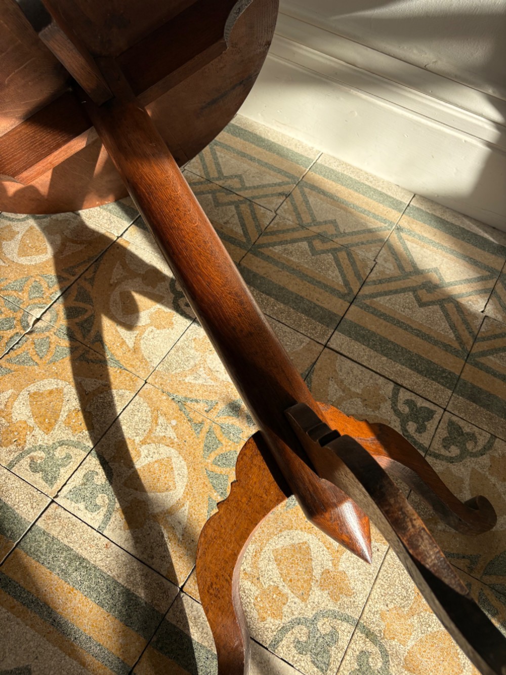 An English Arts and Crafts solid oak wine table featuring a circular top, an under-top support bracket, a central column terminating in a pointed lower finial, and three splayed cabriole legs. View IX