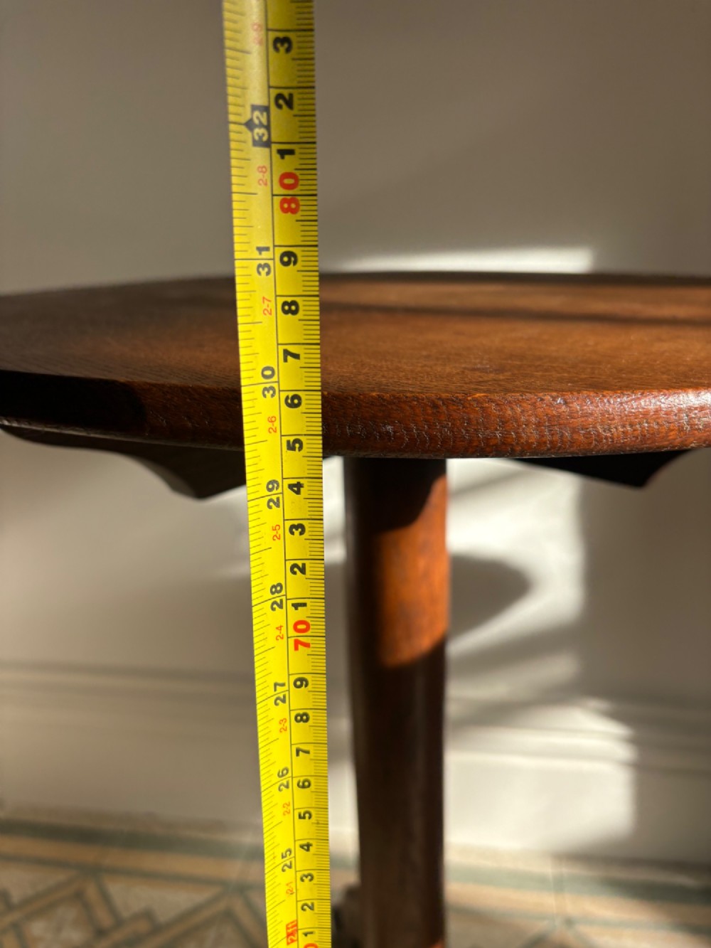 An English Arts and Crafts solid oak wine table featuring a circular top, an under-top support bracket, a central column terminating in a pointed lower finial, and three splayed cabriole legs. View XIII