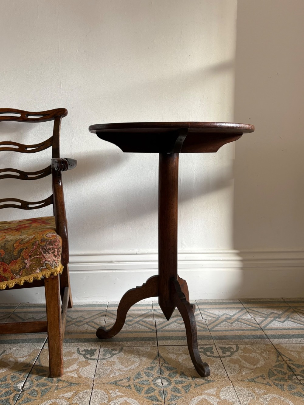 An English Arts and Crafts solid oak wine table featuring a circular top, an under-top support bracket, a central column terminating in a pointed lower finial, and three splayed cabriole legs. View XV