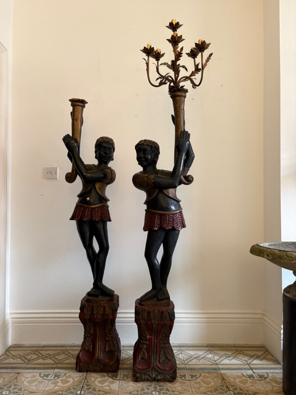 A pair of life-sized Venetian carved wood figure floor lamps featuring gilt and polychrome details, mounted on ornate pedestals with multi-light metal candelabra tops.